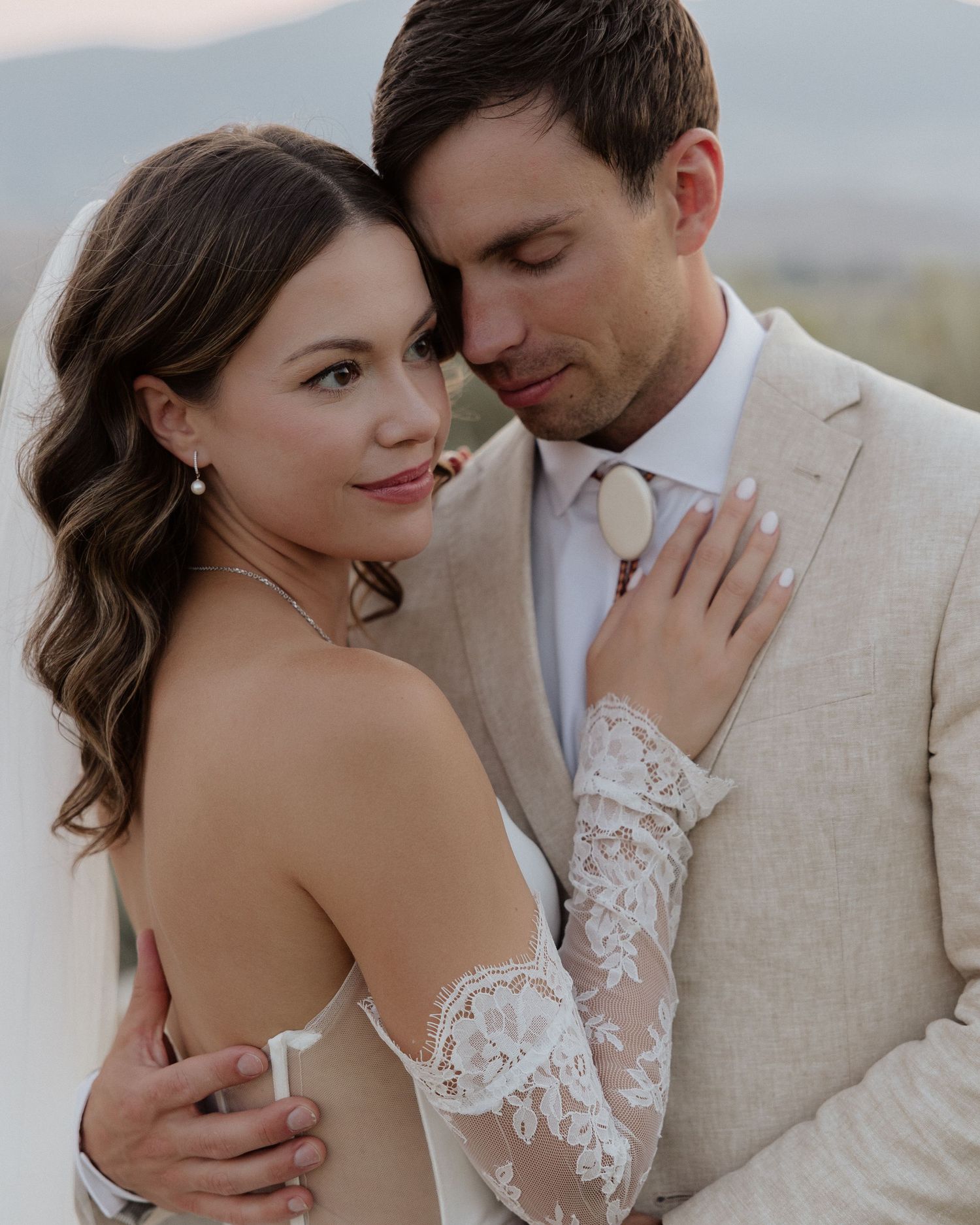 Romantic portrait of newlyweds in soft lighting with mountains in background.