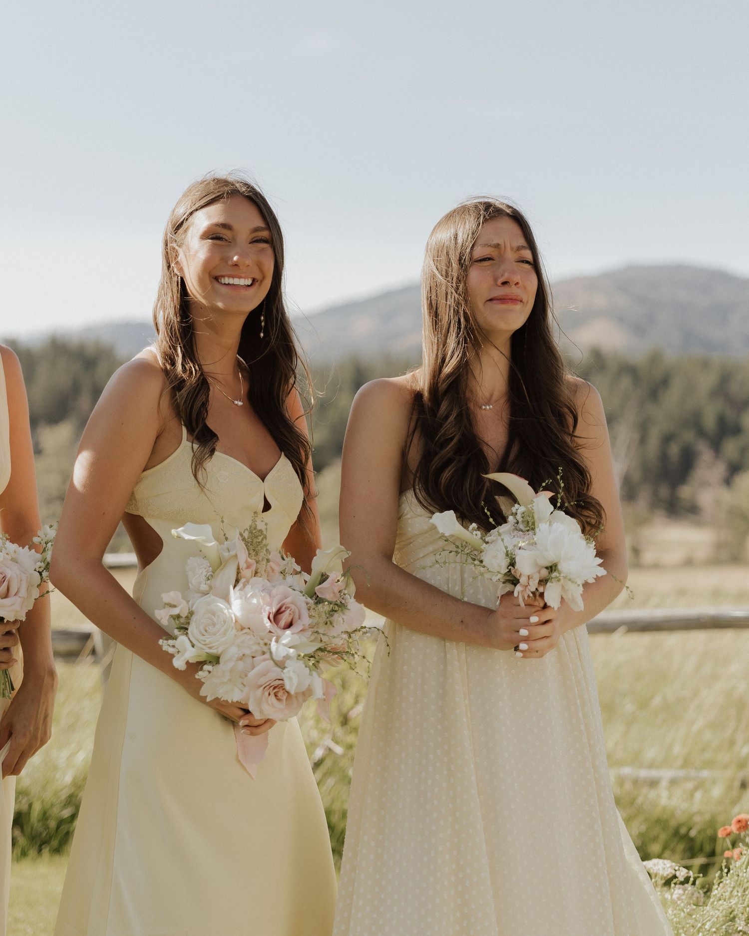 Bridesmaids in pale yellow dresses holding white bouquets pose outdoors against a mountain backdrop.