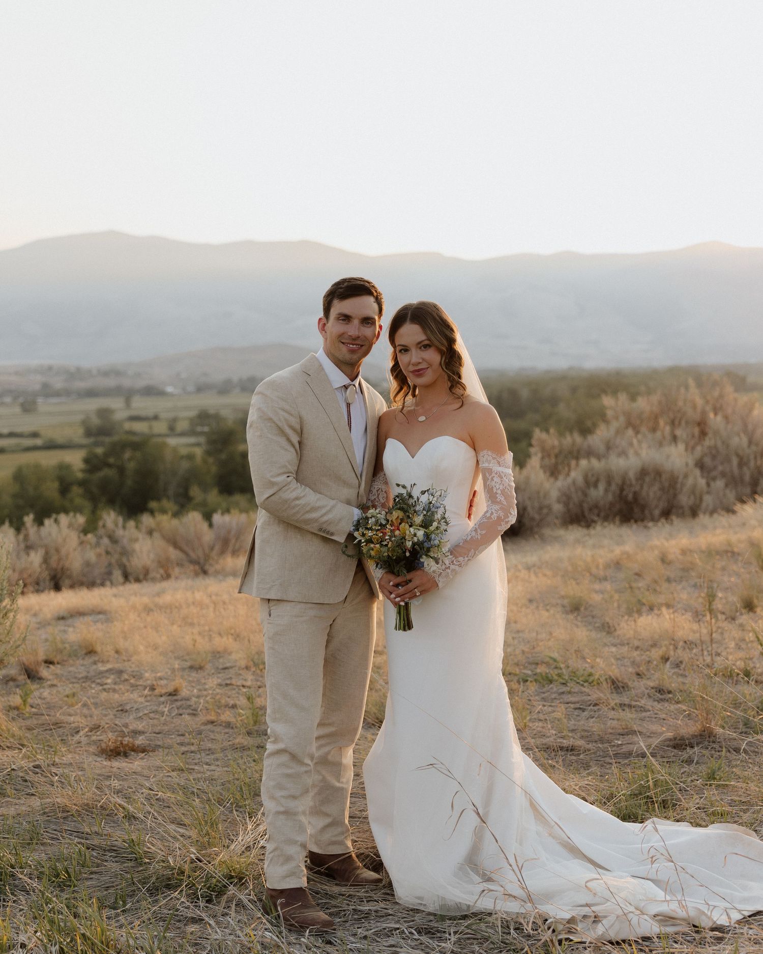 Wedding portrait of couple standing on desert hillside with mountain range in background.