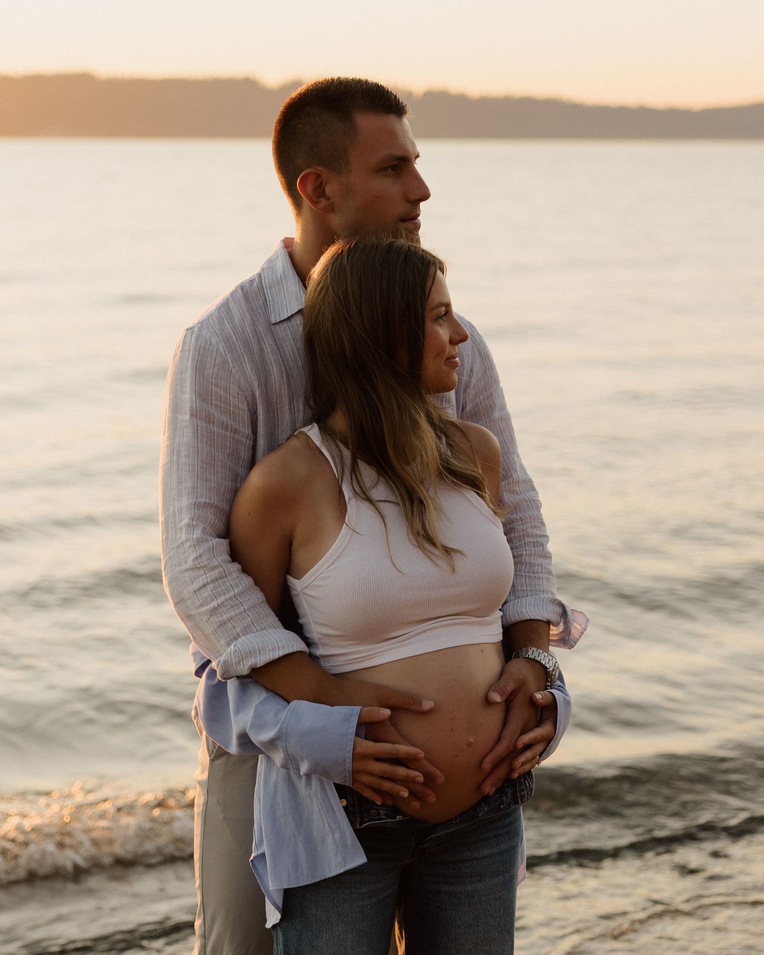 Intimate maternity pose against sunset ocean backdrop.