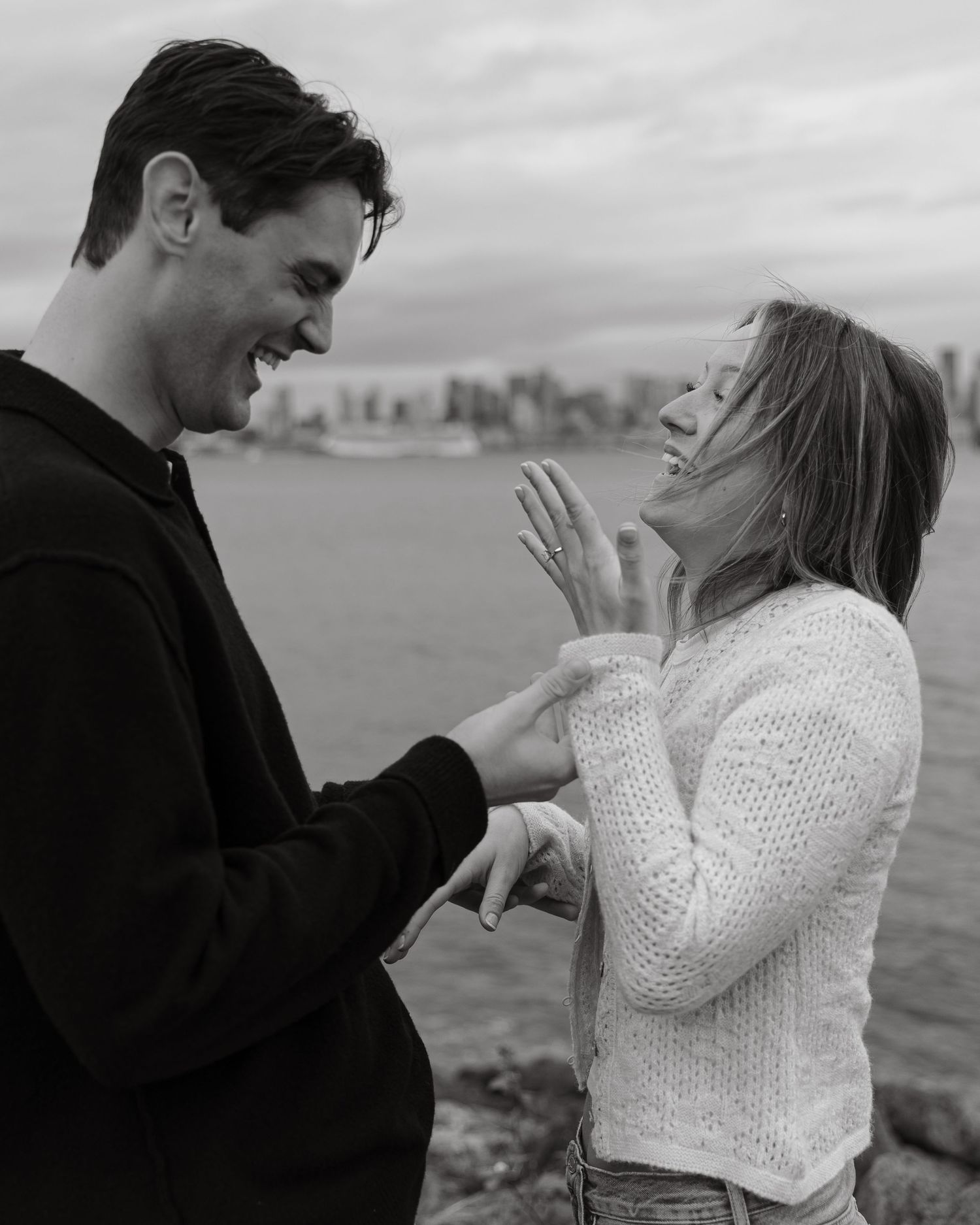 A couple shares a joyful moment together by the waterfront with a city skyline in the background.