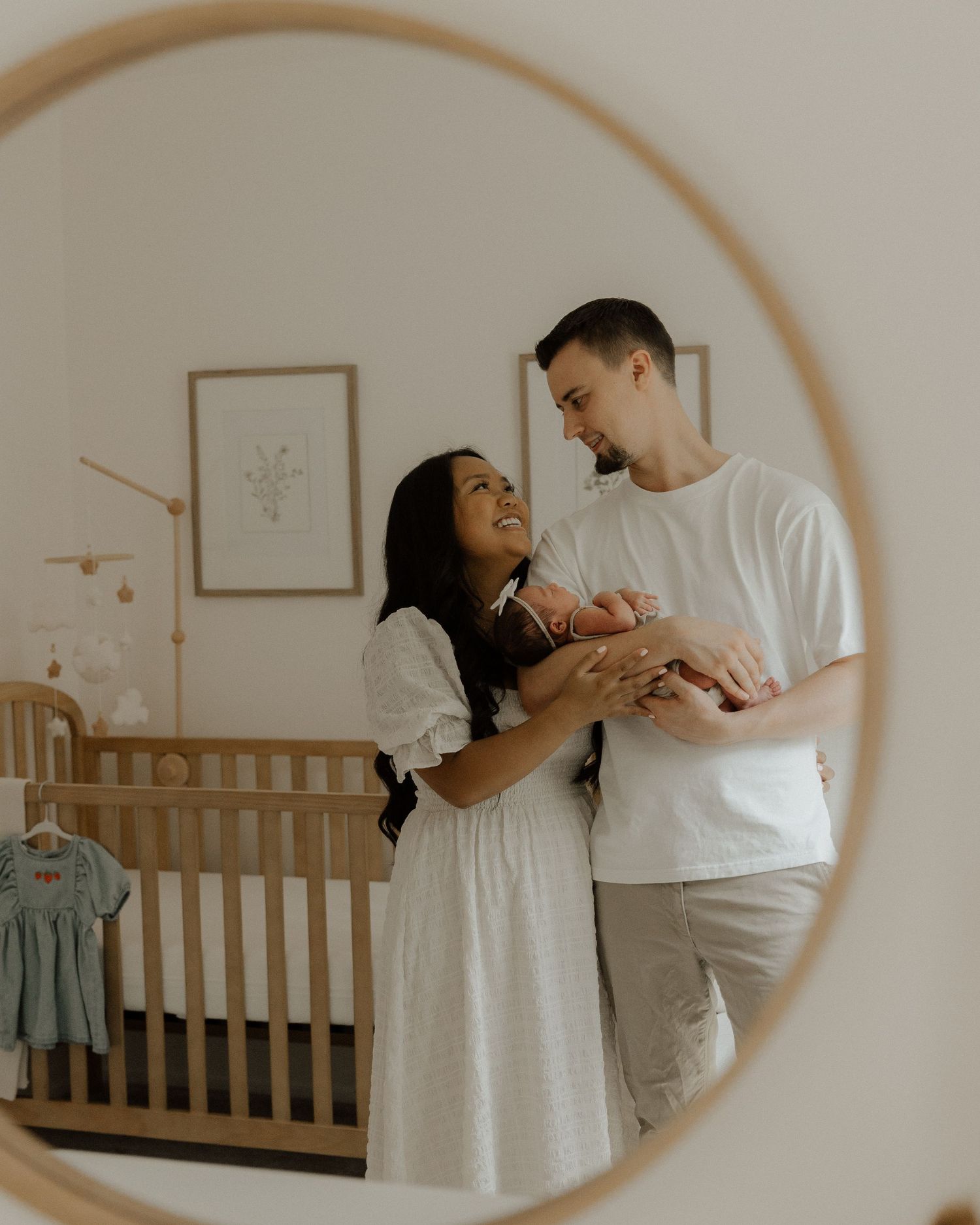 Tender moment captured in mirror reflection as couple shares intimate moment with baby in nursery.