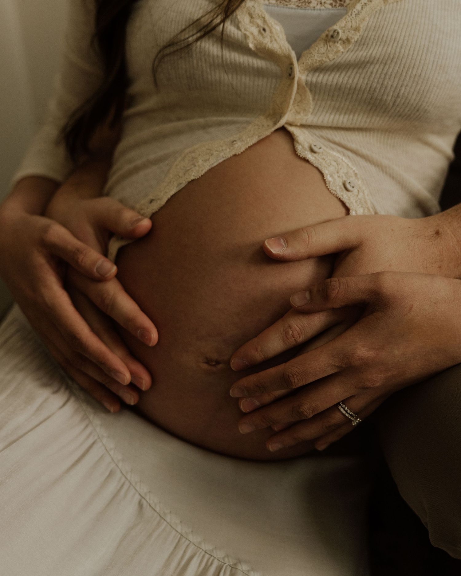 Close-up shot of hands cradling pregnant belly in soft, natural lighting.