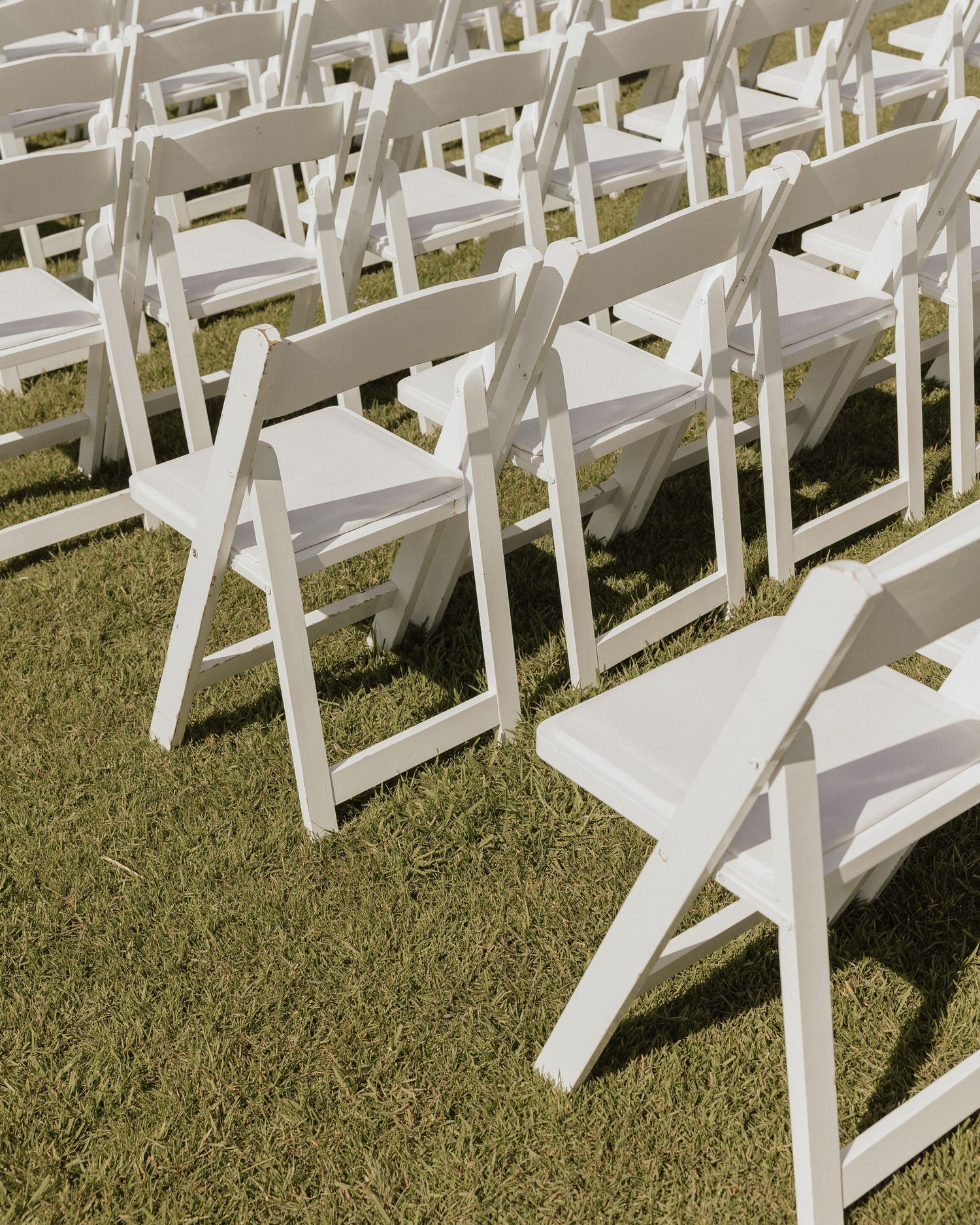 Rows of white folding chairs set up on grass for an outdoor wedding ceremony.