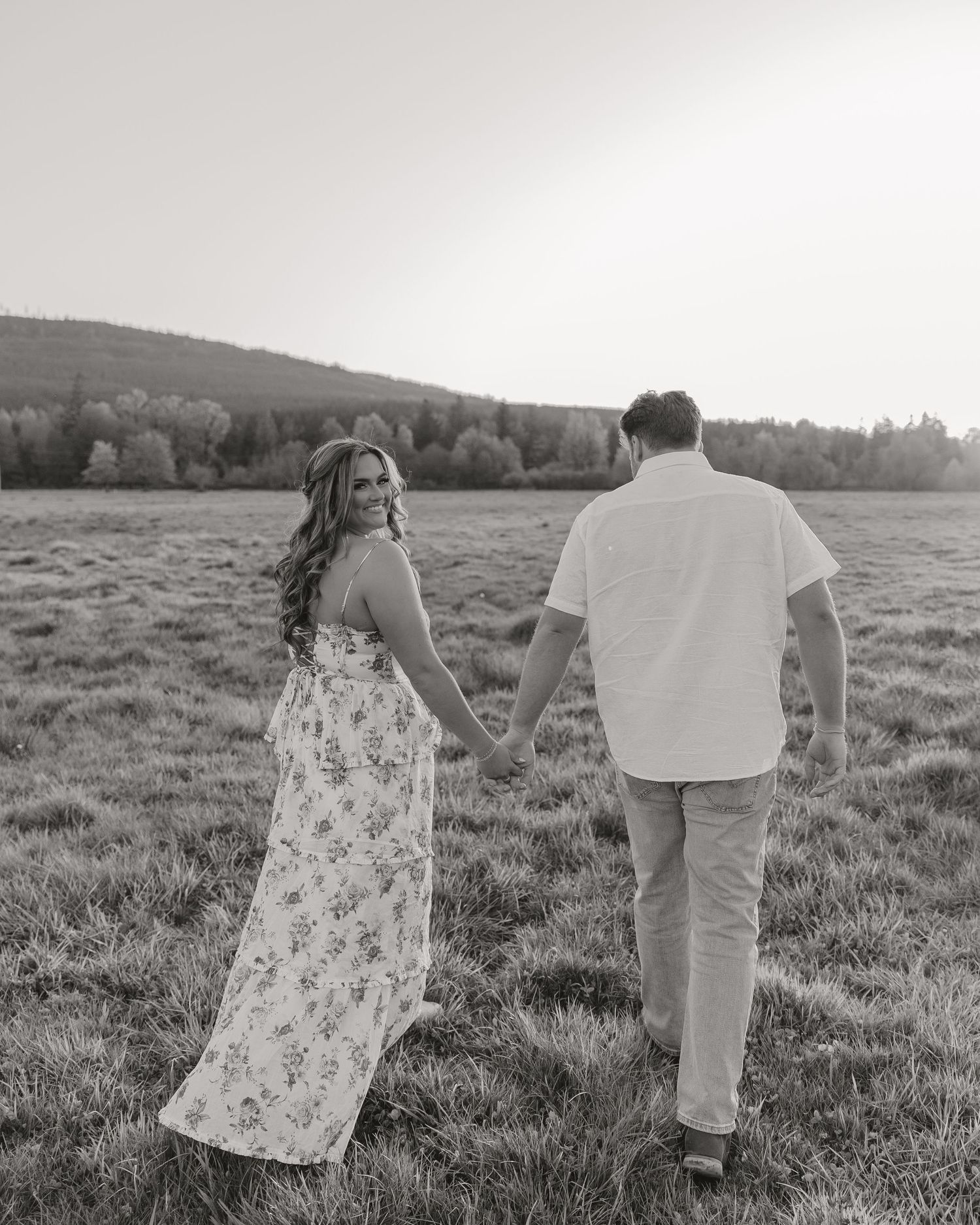 Couple walking hand in hand through grassy meadow in black and white photo.