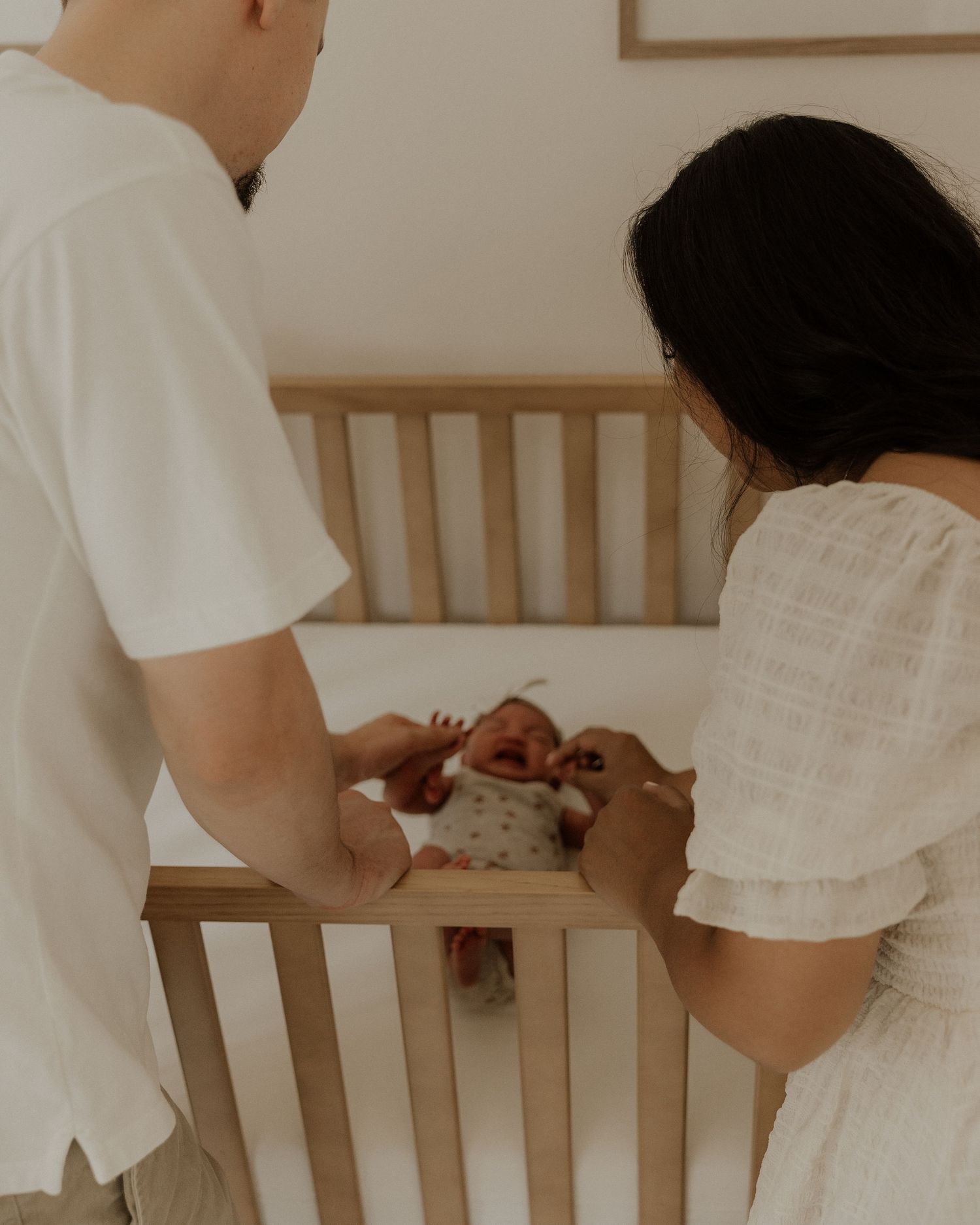 Parents leaning over wooden crib together looking at their newborn baby.