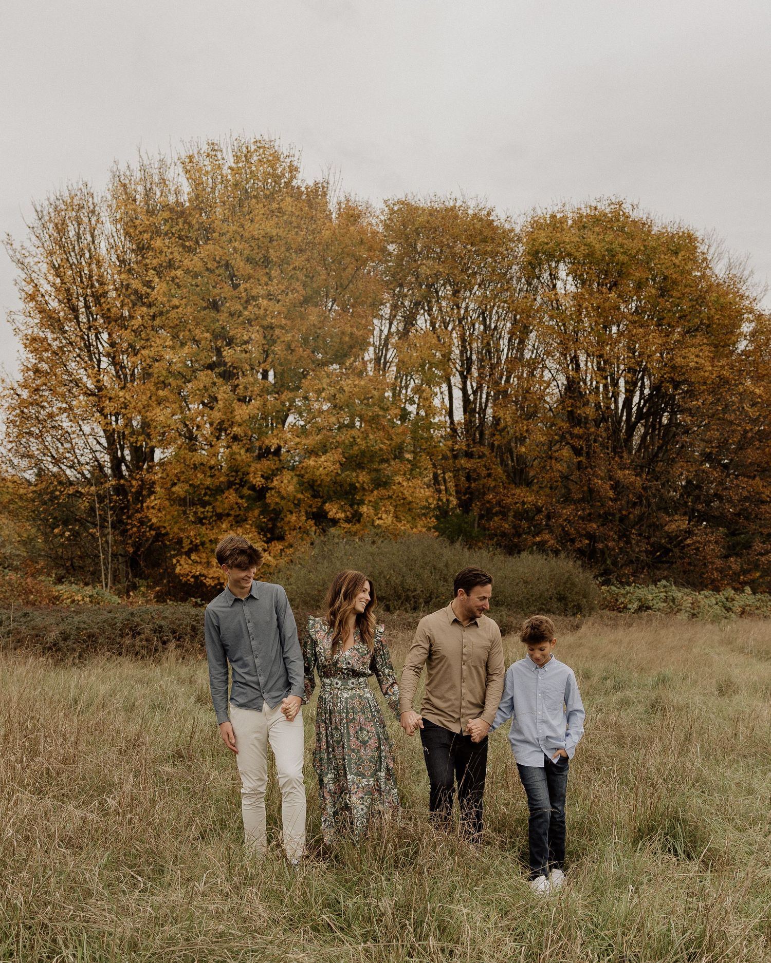 Casual group portrait against autumn trees in a grassy meadow during golden hour.