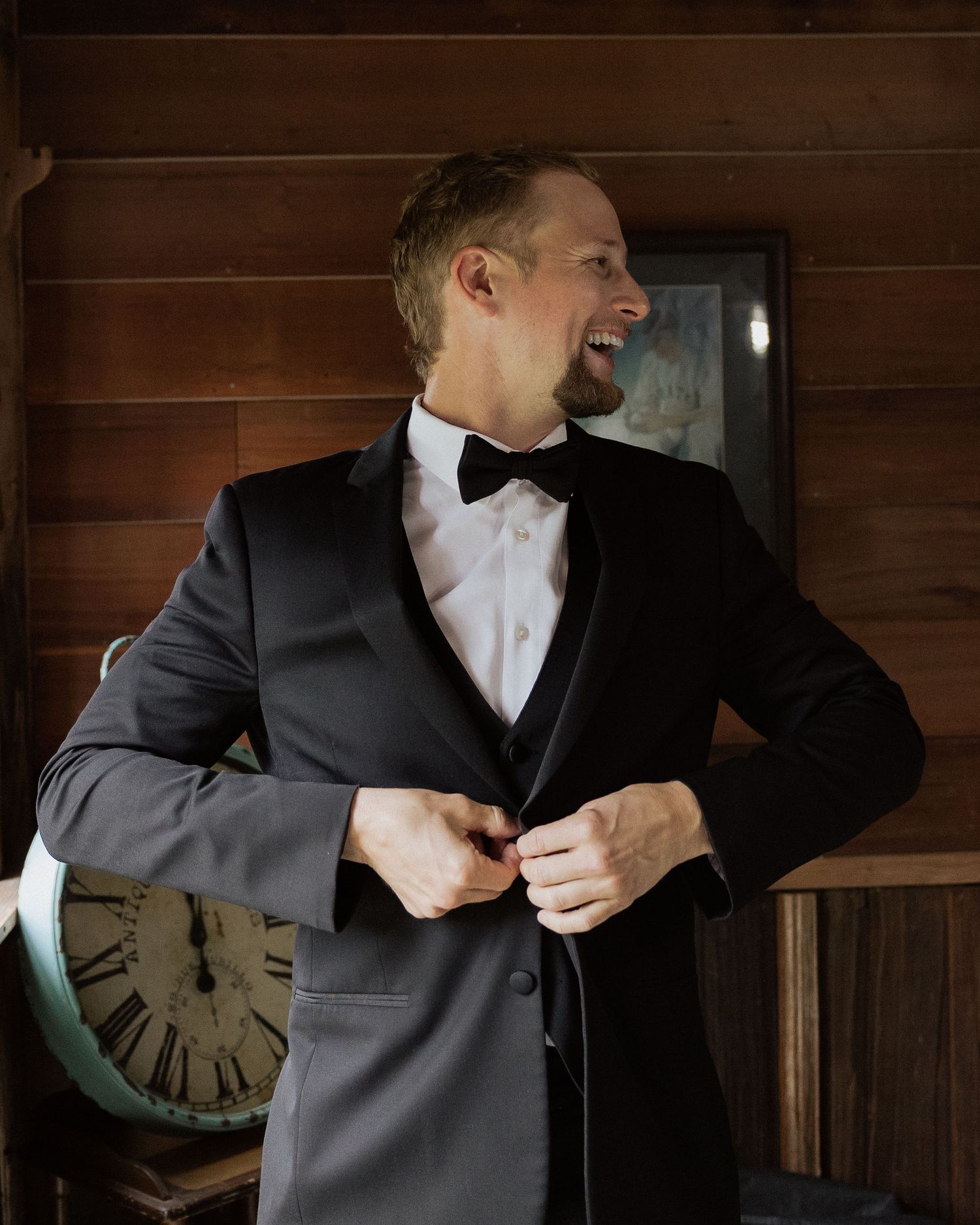 Person in formal black tuxedo getting dressed in rustic room with vintage clock.