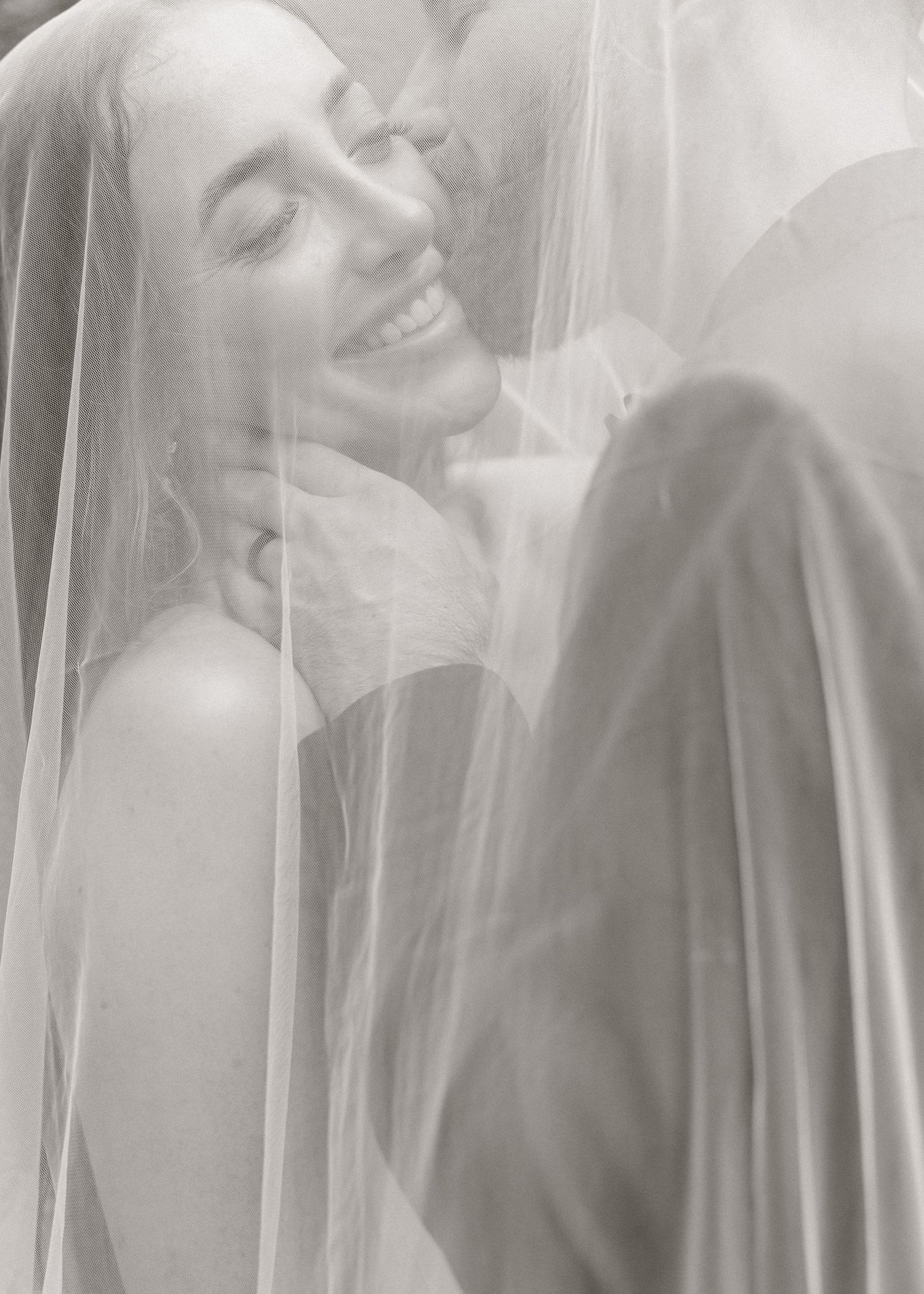 Bride smiling under veil with groom in black and white wedding portrait photo.