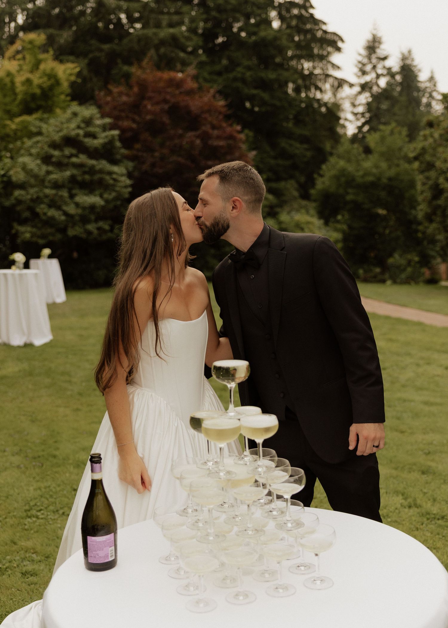 Bride and groom kiss behind a champagne tower at their outdoor wedding reception.