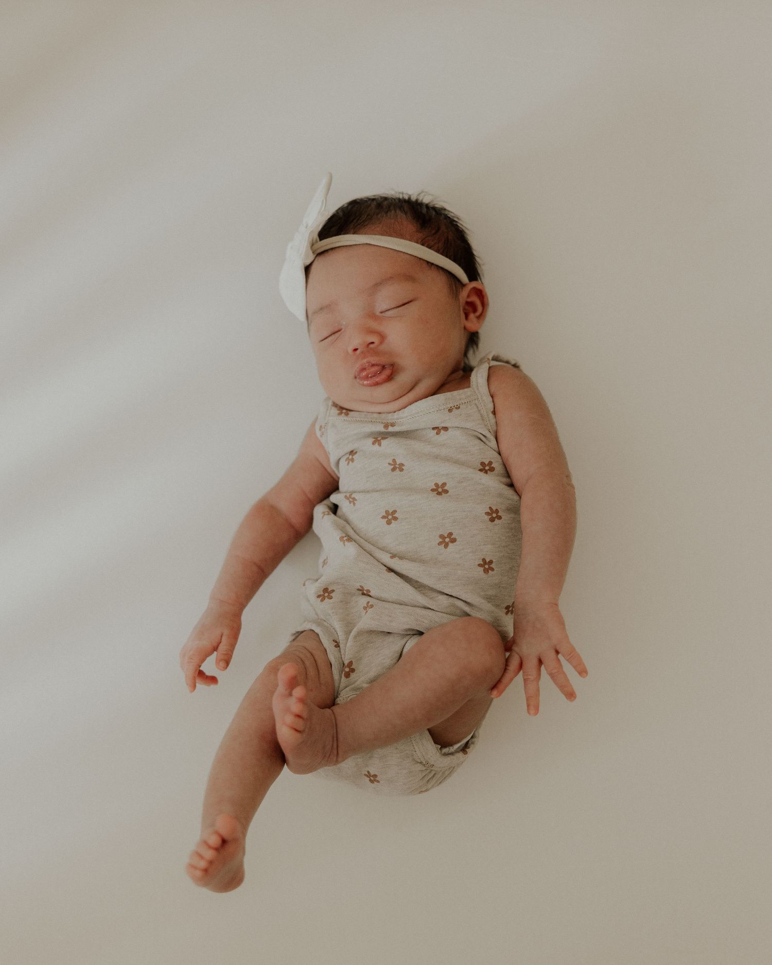 Sleeping newborn wearing floral onesie and white headband on white background.