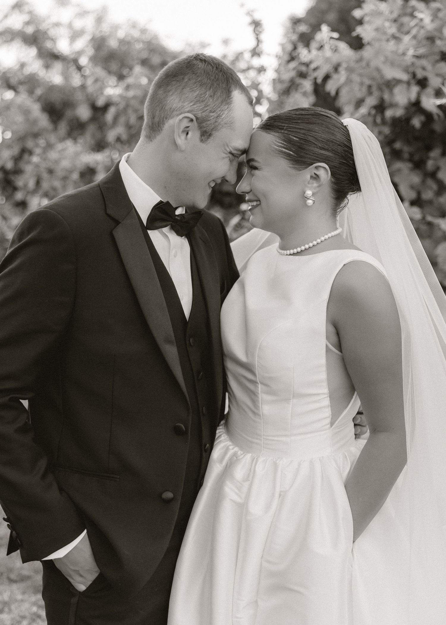 Black and white portrait of smiling bride and groom gazing at each other in vineyard setting.