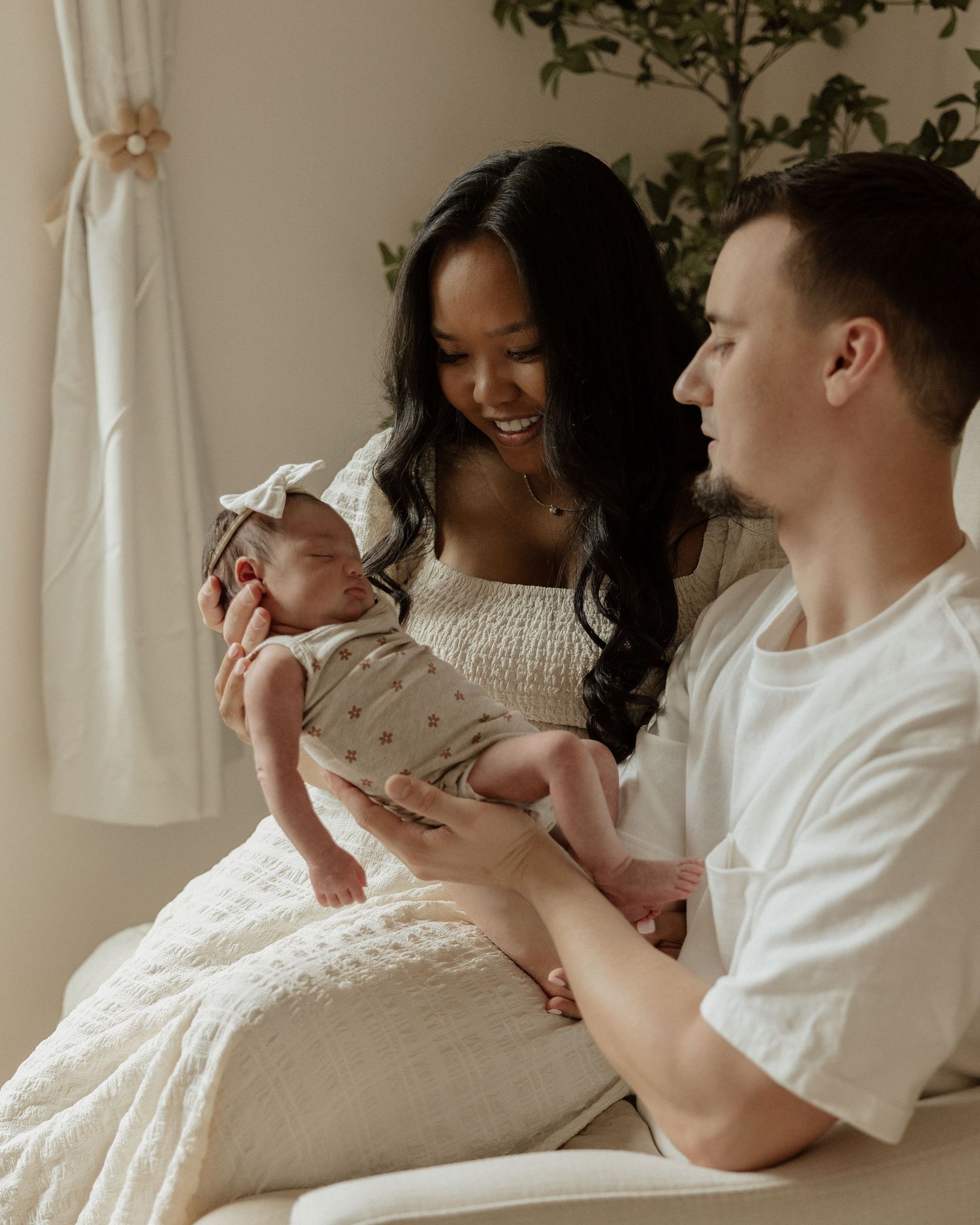 New parents sharing an intimate moment with their newborn baby on a white couch in a bright, minimalist nursery.