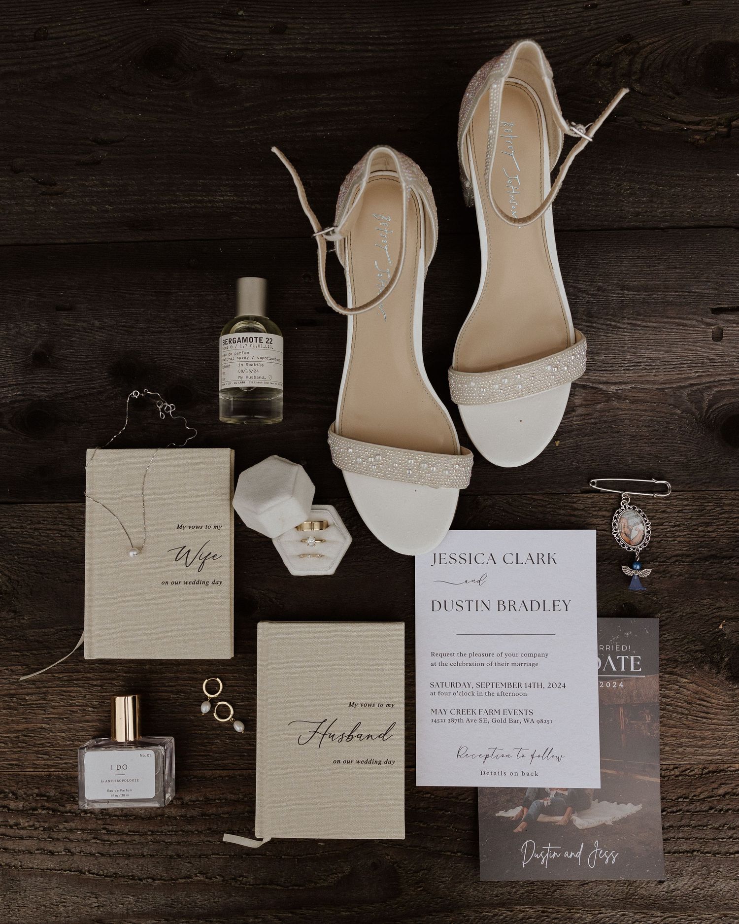 Wedding details flatlay with white shoes, invitations, perfume and rings on dark wood.