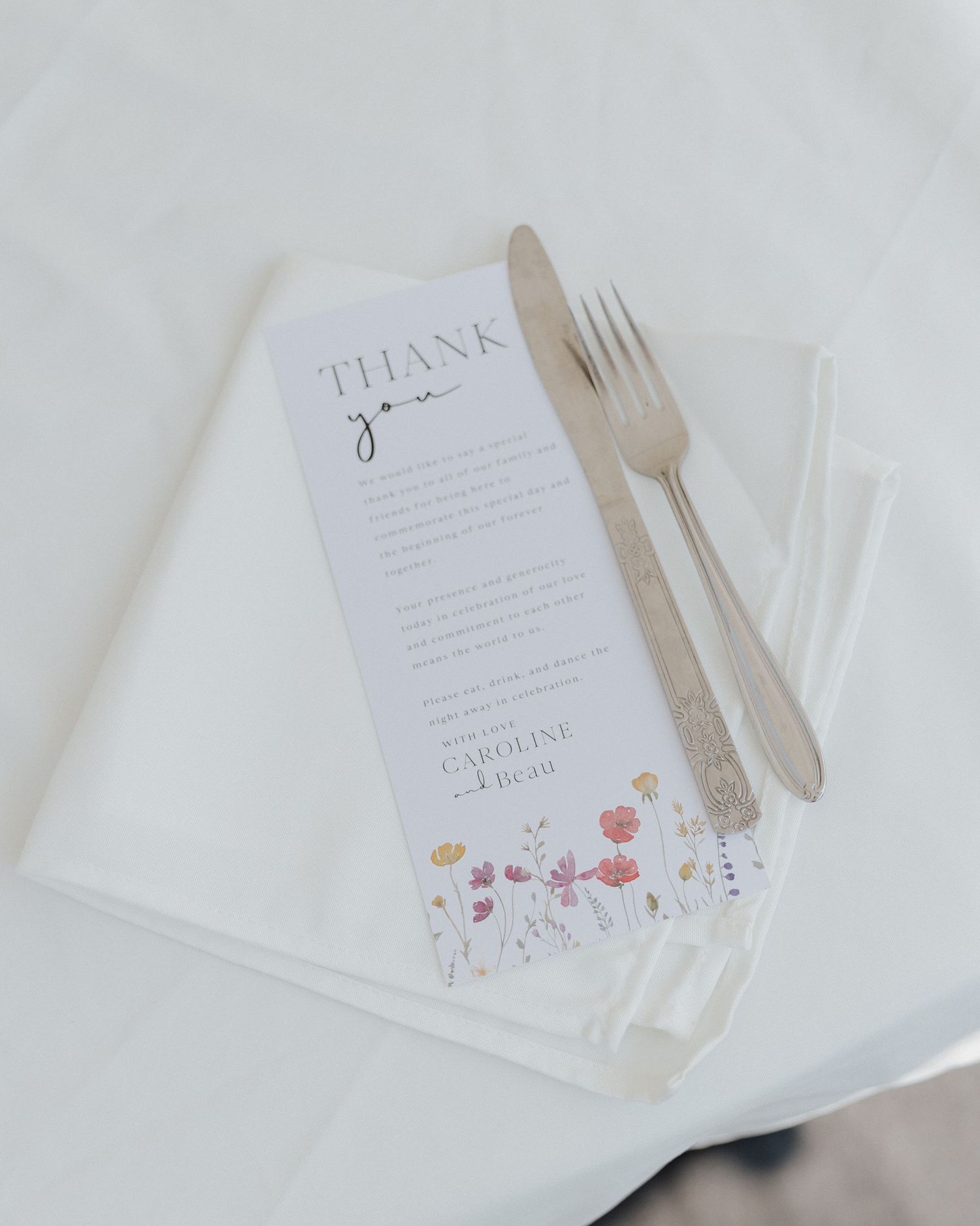 Wedding menu card with floral design placed on white napkin with wooden utensils.