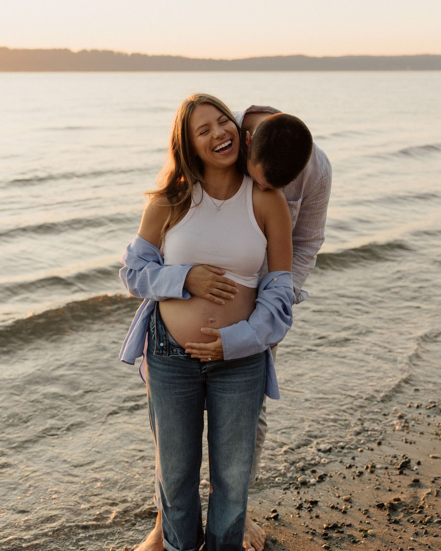 An intimate maternity photo of a couple embracing on a beach at sunset.