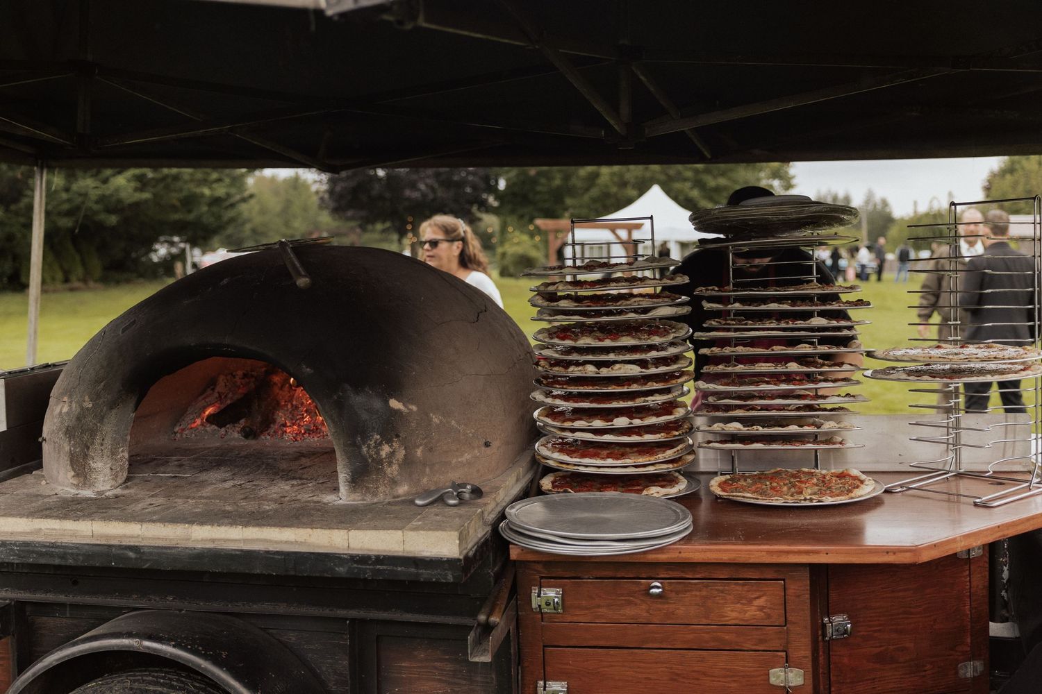 Large outdoor pizza oven with stacks of pizza trays beside it.