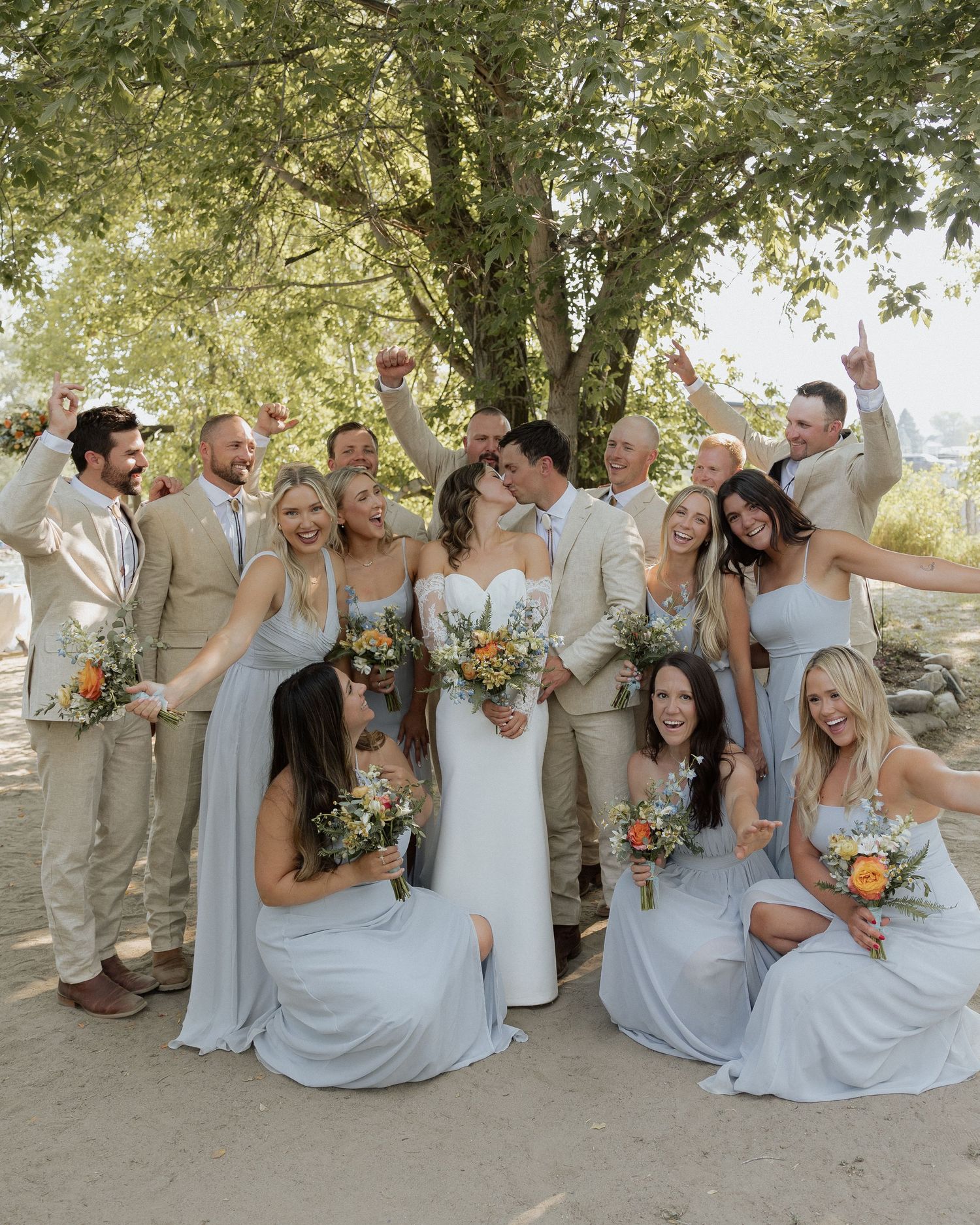 Wedding party in beige suits and blue dresses posing together outdoors.