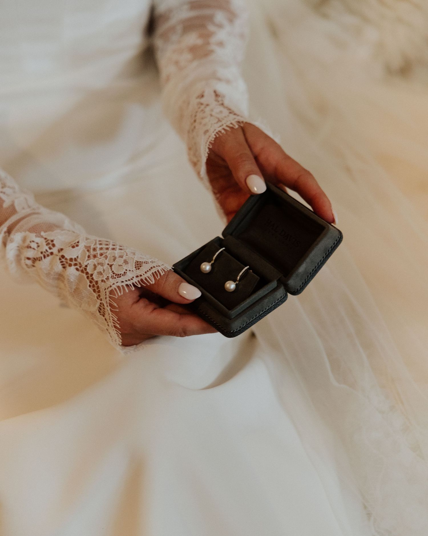 Hands in lace sleeves holding a small black ring box.