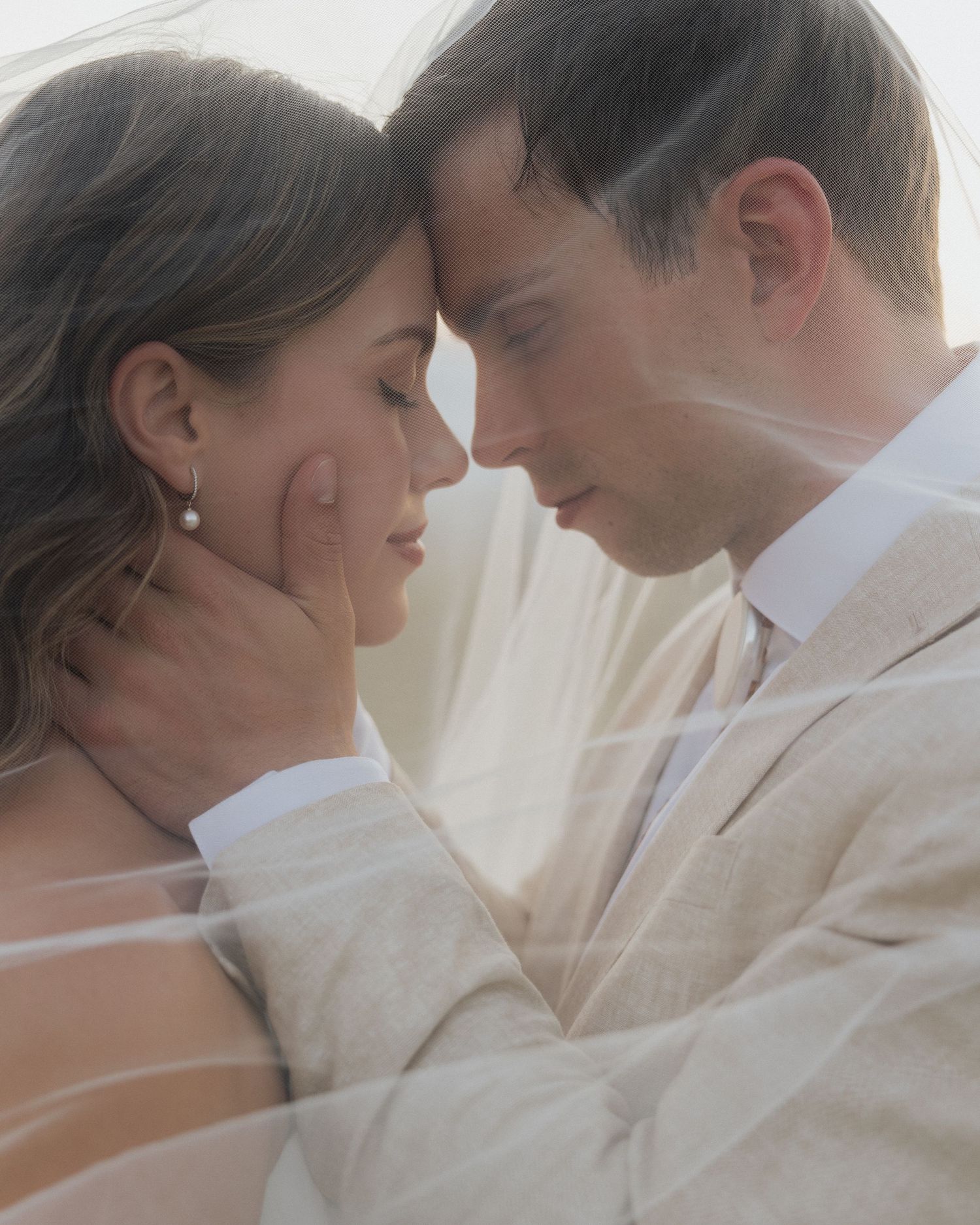 Romantic close-up moment between couple in soft lighting with veil detail.