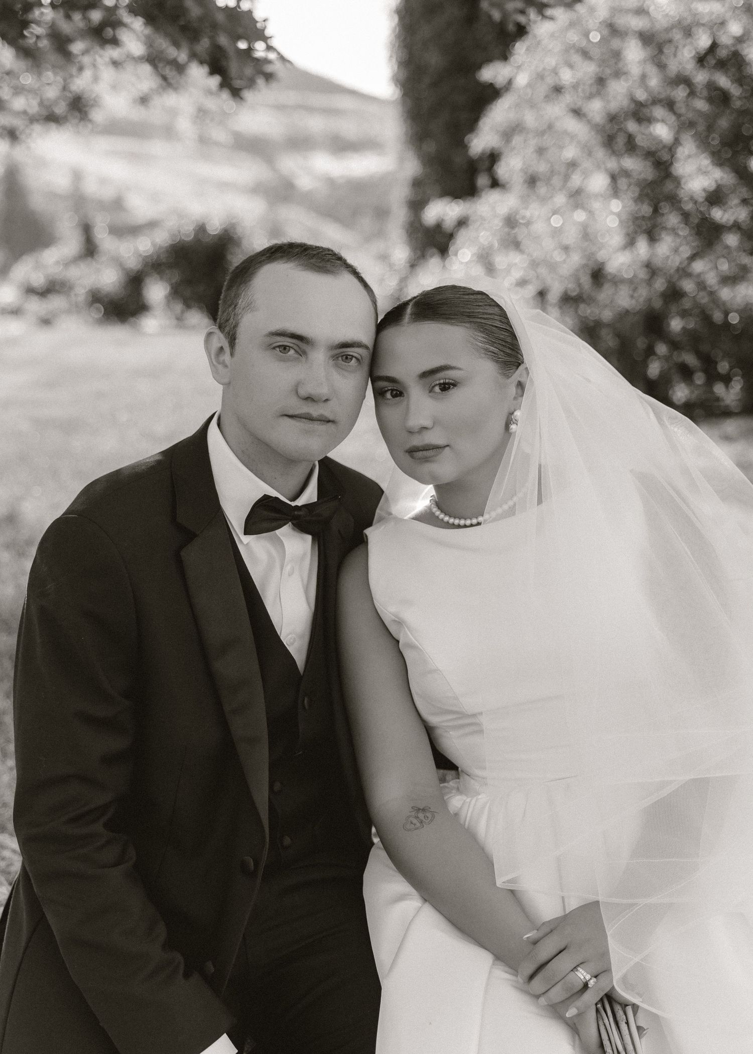 Black and white portrait of bride and groom sitting together in garden on wedding day.