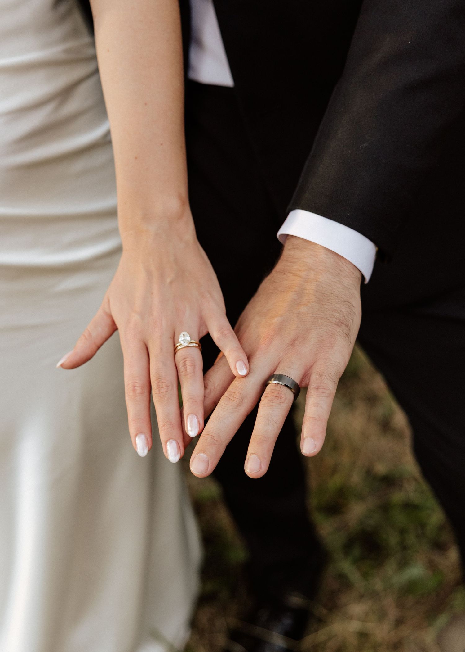 Close-up of bride and groom displaying wedding rings, featuring diamond engagement ring and dark tungsten band.