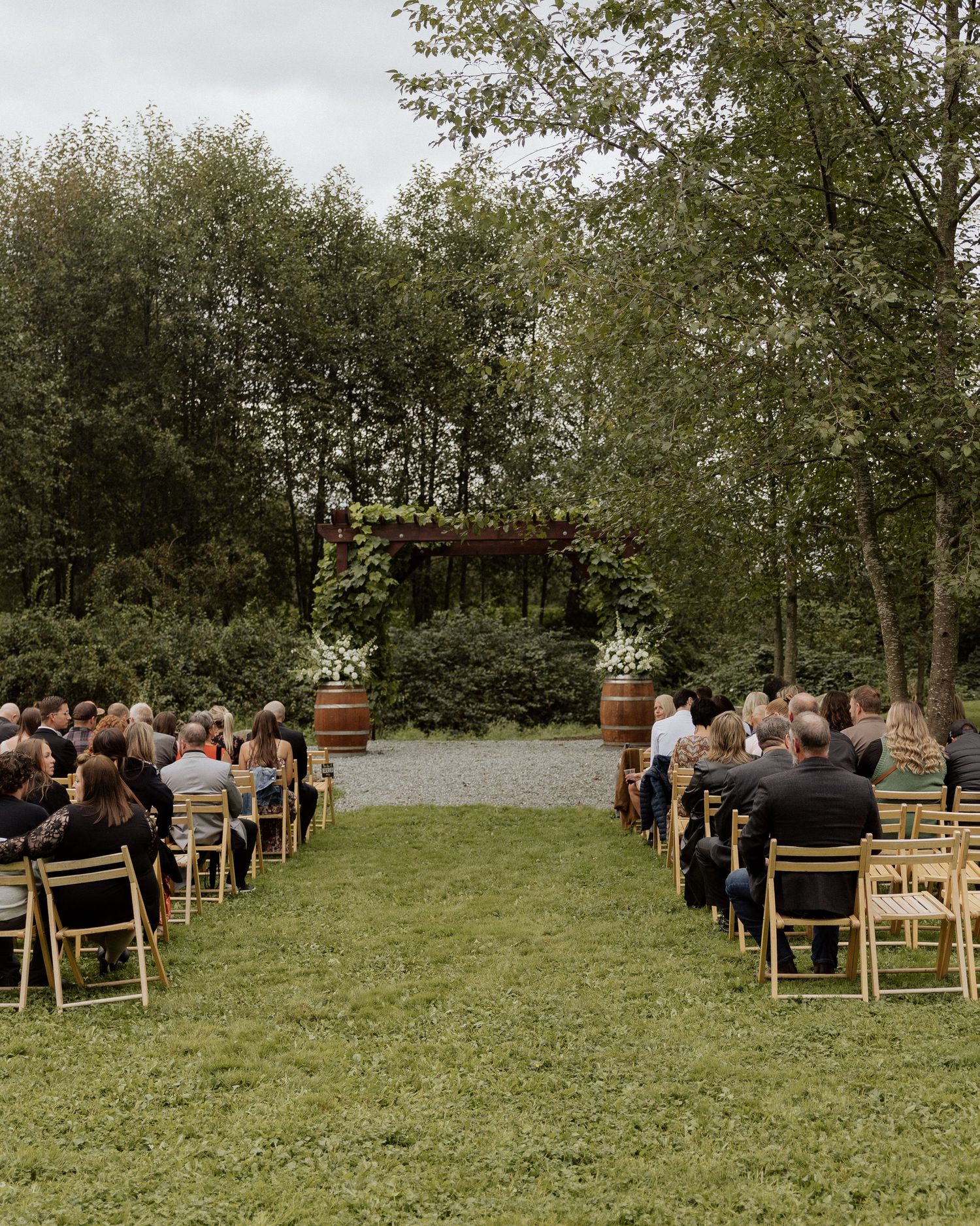 Outdoor wedding ceremony setup with wooden chairs and floral arch surrounded by trees.