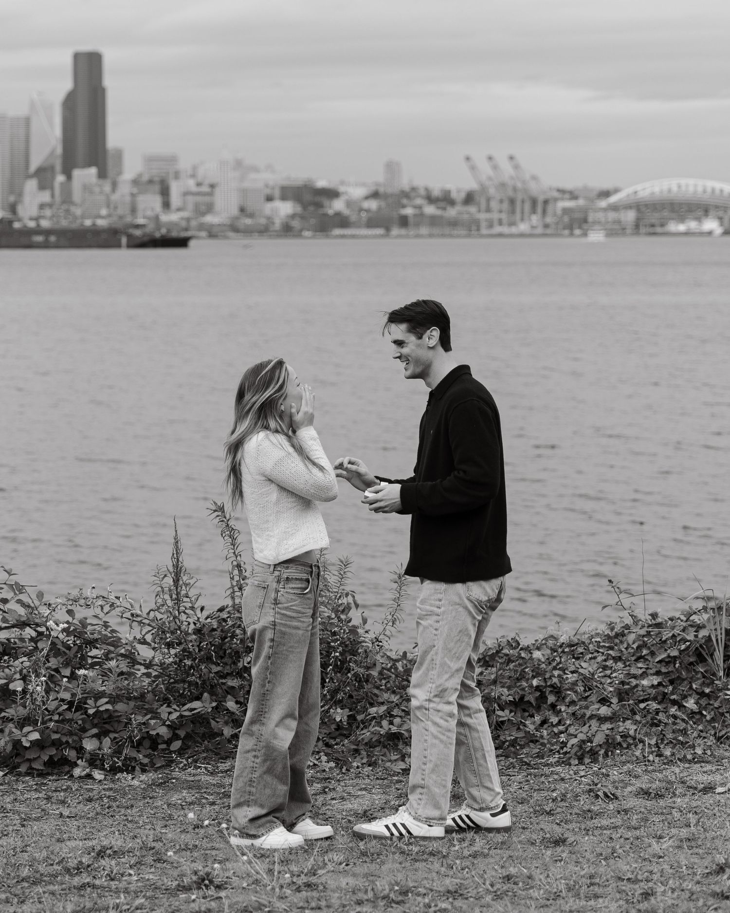 A couple shares an intimate moment with a city skyline backdrop during what appears to be a proposal.