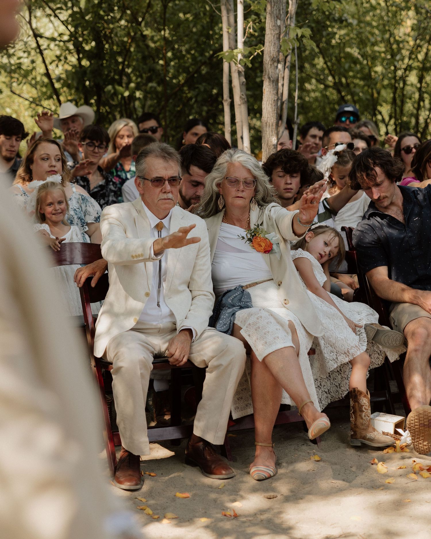 Wedding guests seated outdoors on wooden benches watching the ceremony unfold.