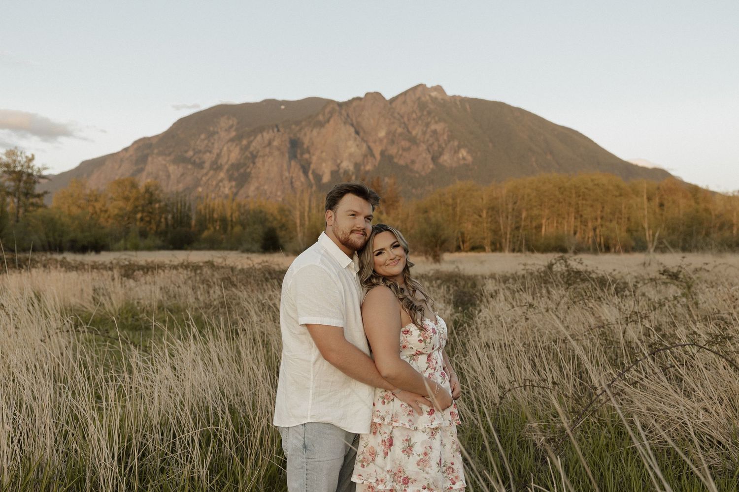 Romantic couple embracing in field with mountain landscape behind them.