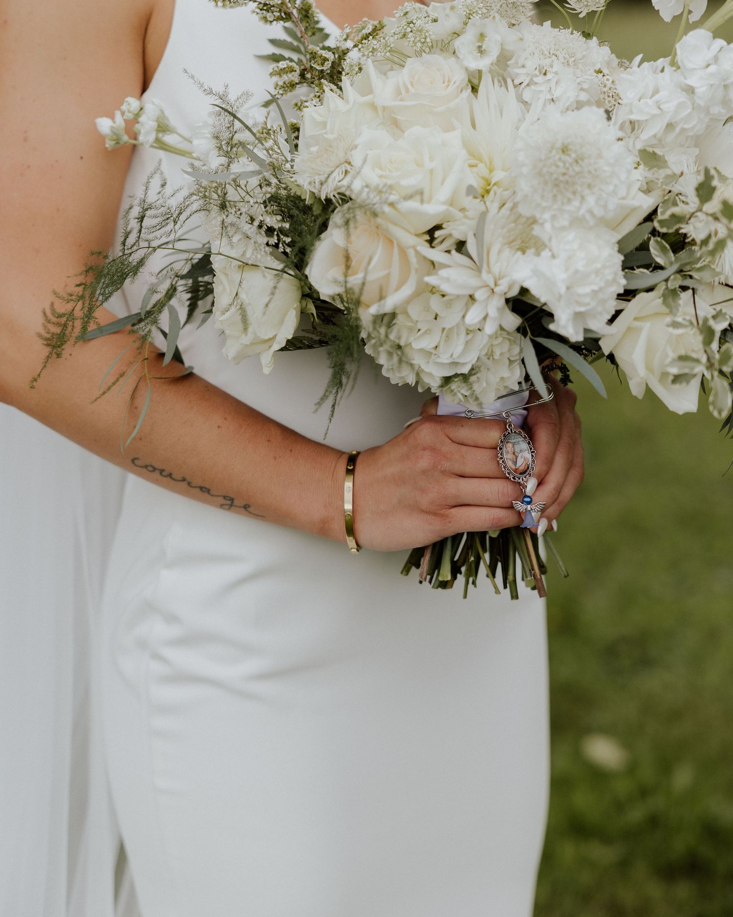 Close up of bridal bouquet with white flowers and greenery, showing gold bracelet and ring details.