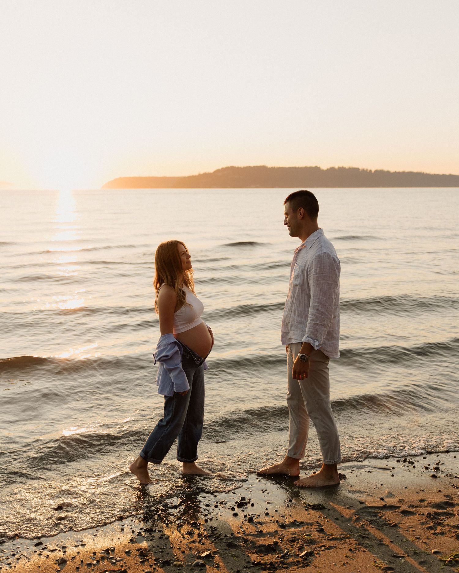 Maternity beach portrait with glowing sunset over water.