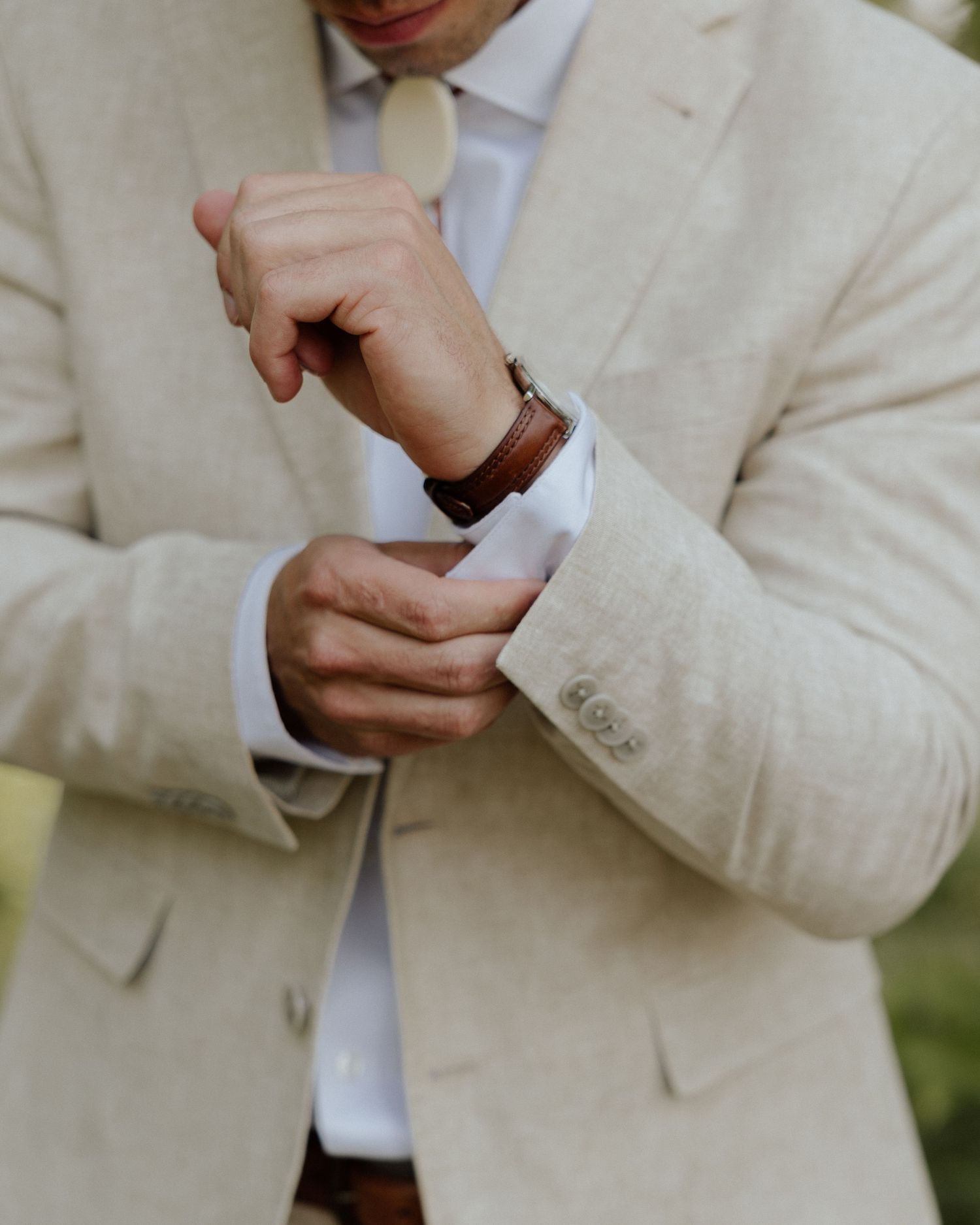 Person in beige suit adjusting white dress shirt cuff.
