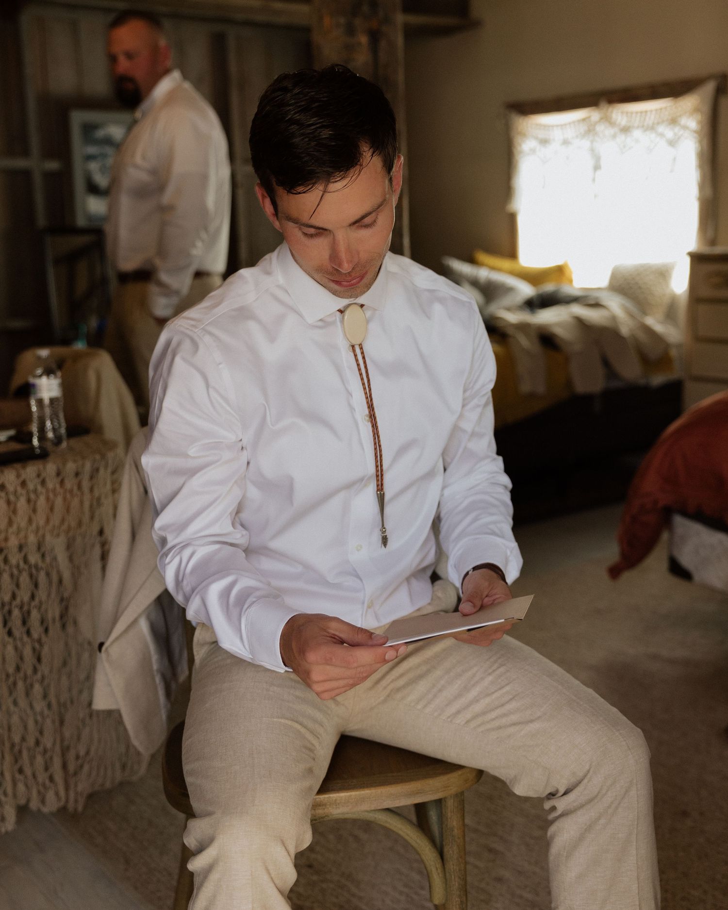 Someone in formal attire with a bolo tie reads while seated on a wooden chair.