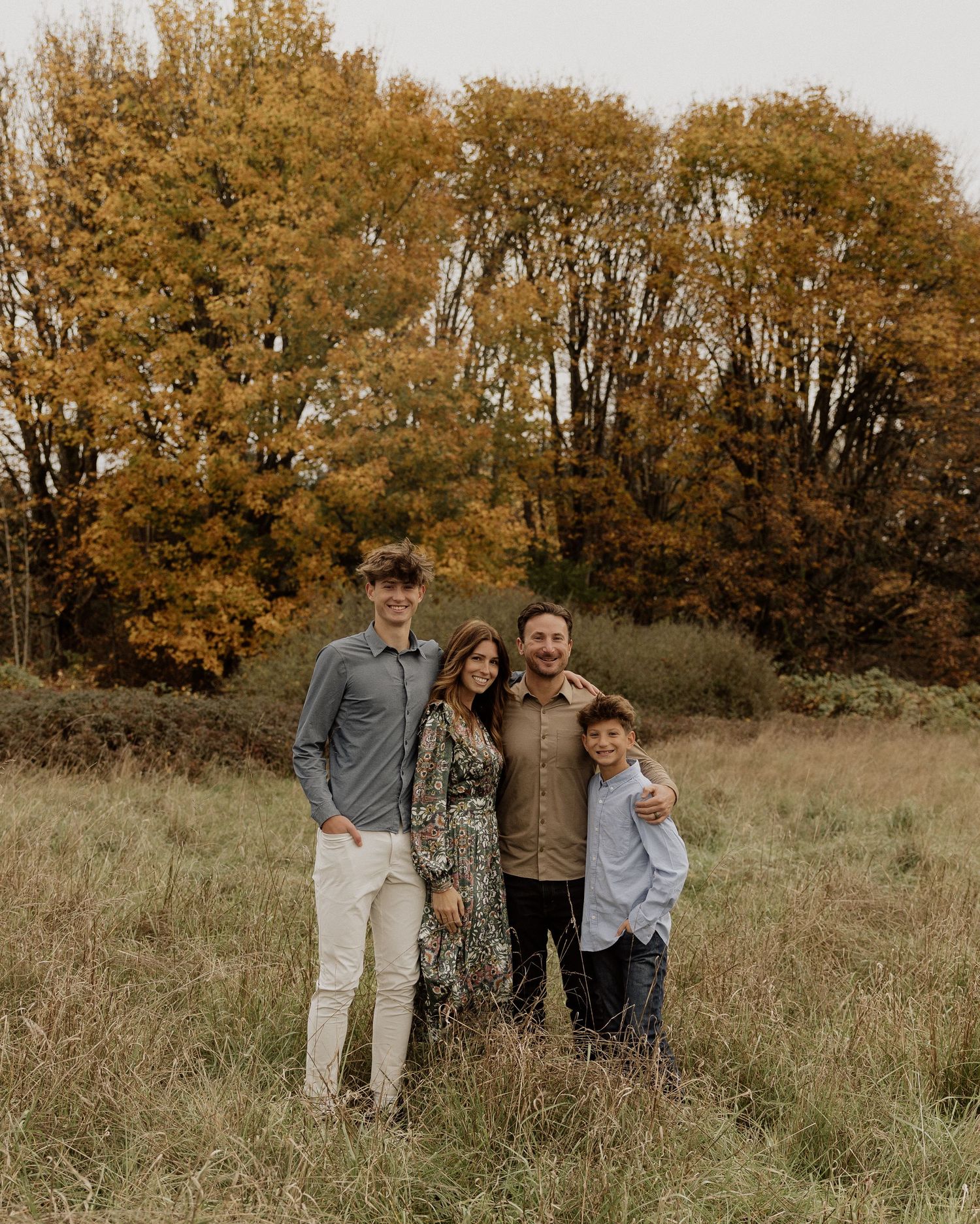 Family poses together in a field with golden autumn trees in the background.
