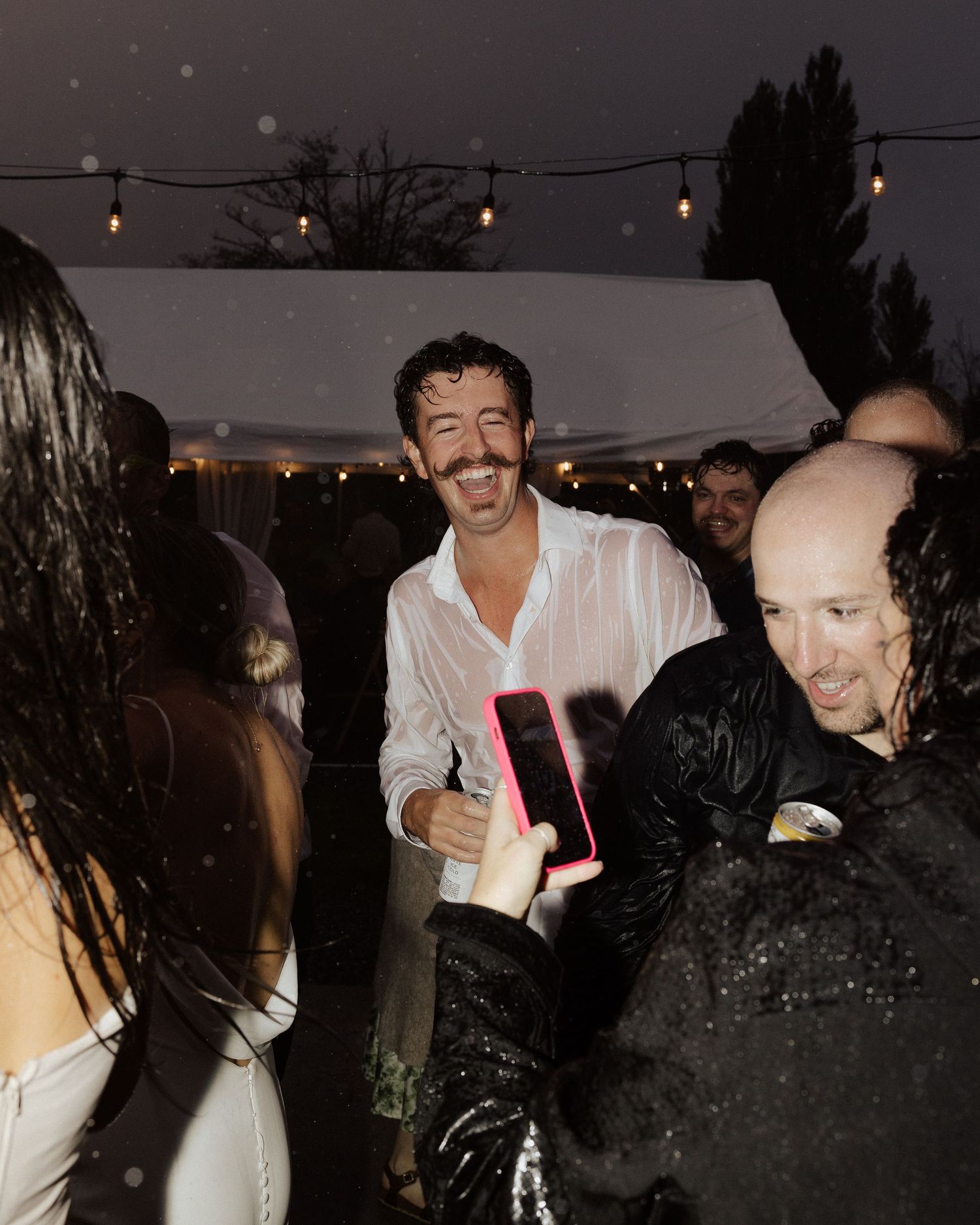 A lively outdoor wedding reception with string lights and guests dancing at night.