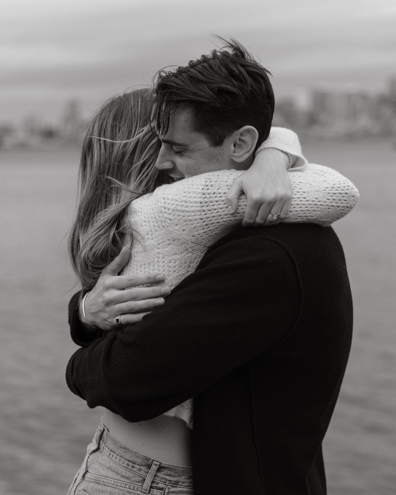 Intimate black and white portrait of couple embracing by waterfront.