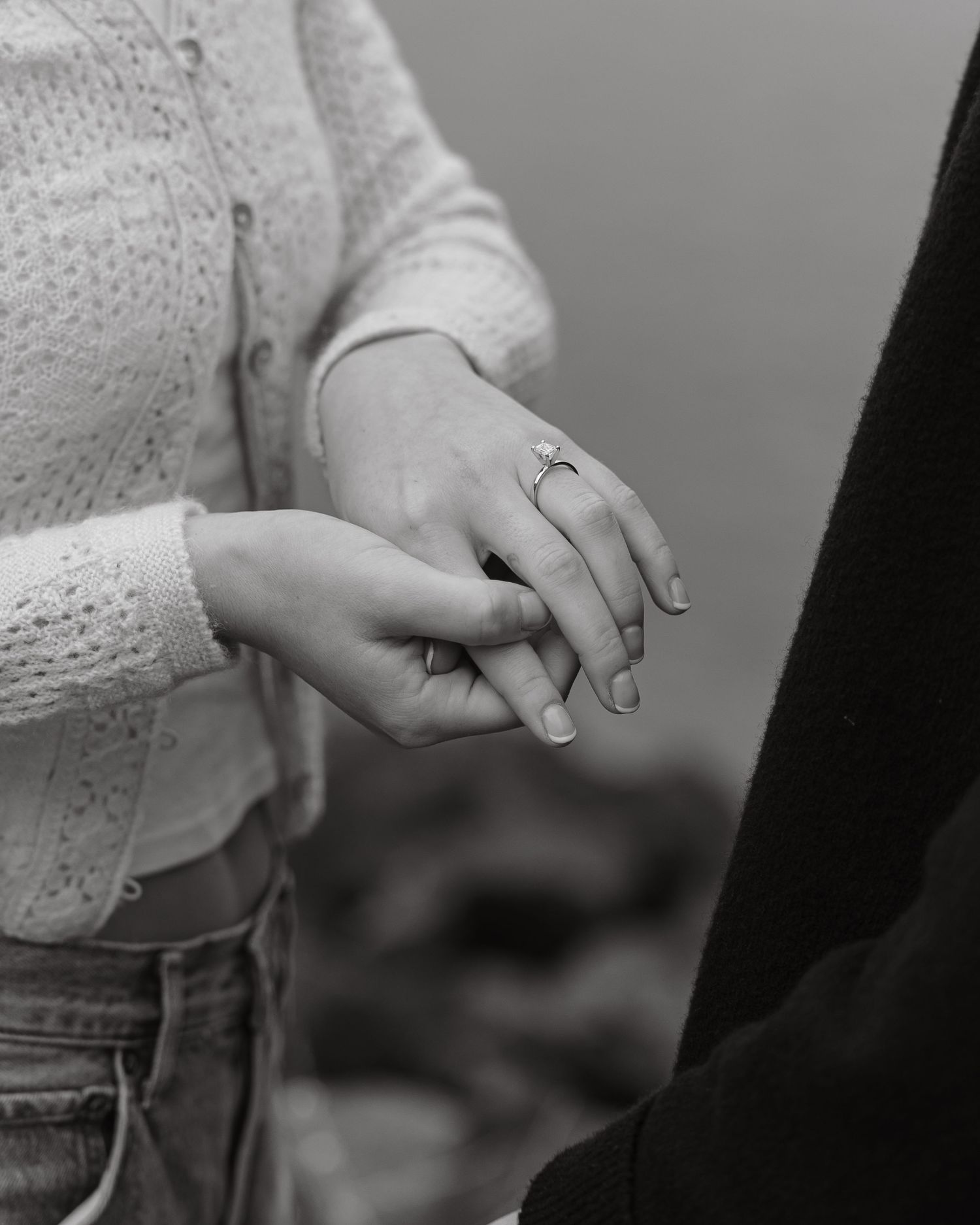 Close-up shot of hands displaying a new engagement ring against a blurred background.