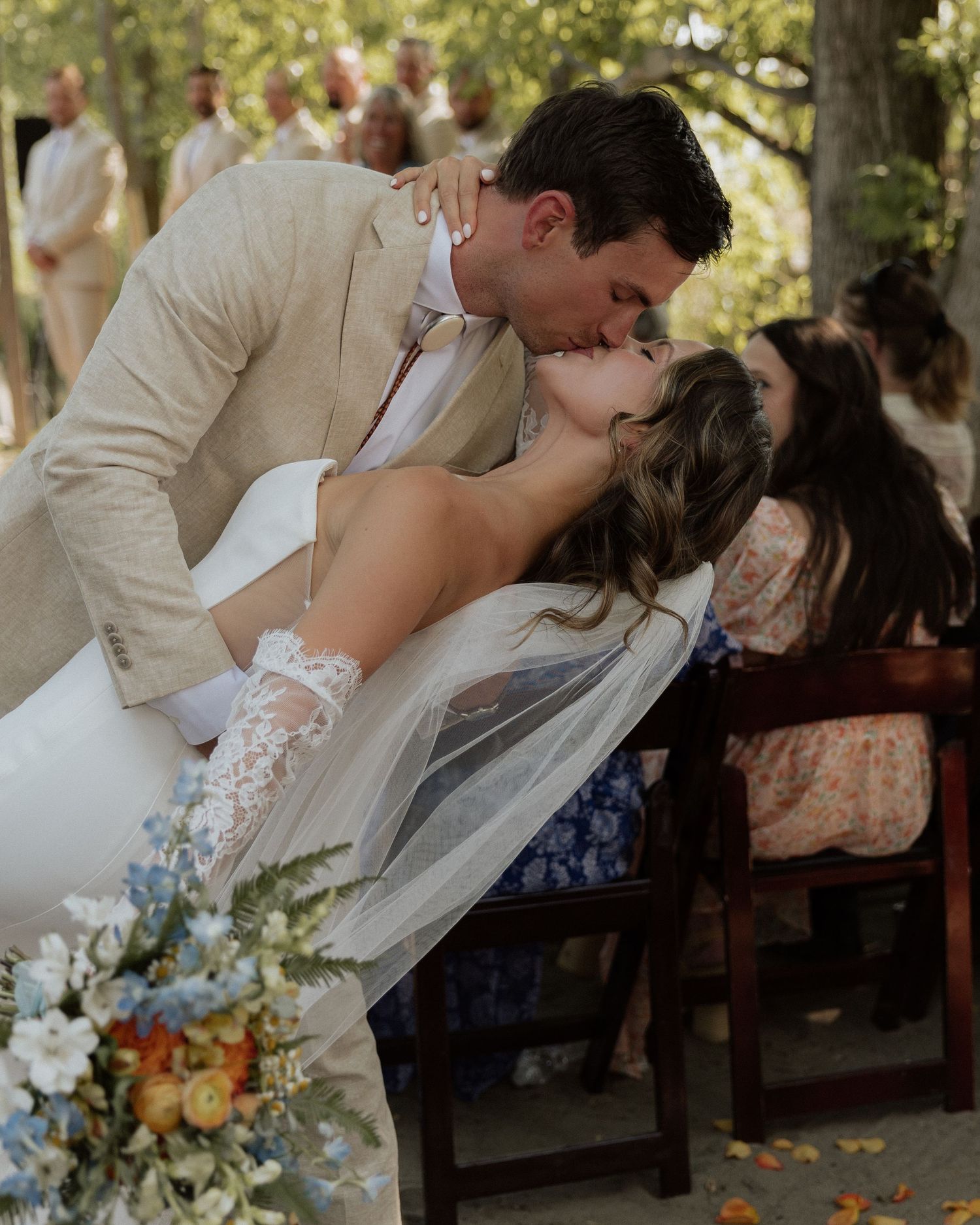 A romantic dip kiss between newlyweds during their outdoor wedding celebration.