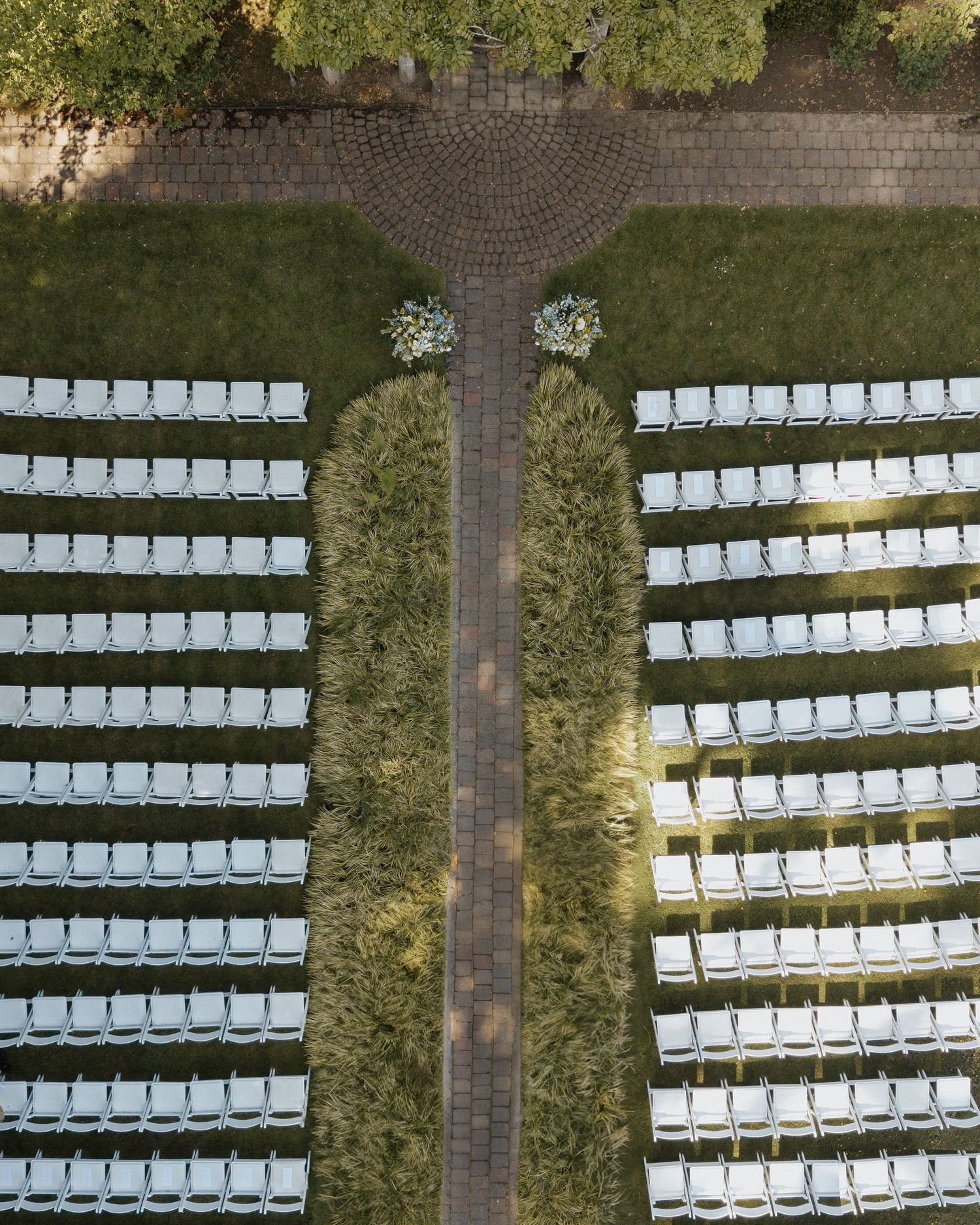 Aerial view of outdoor wedding ceremony setup with rows of white chairs and a central aisle on green lawn.