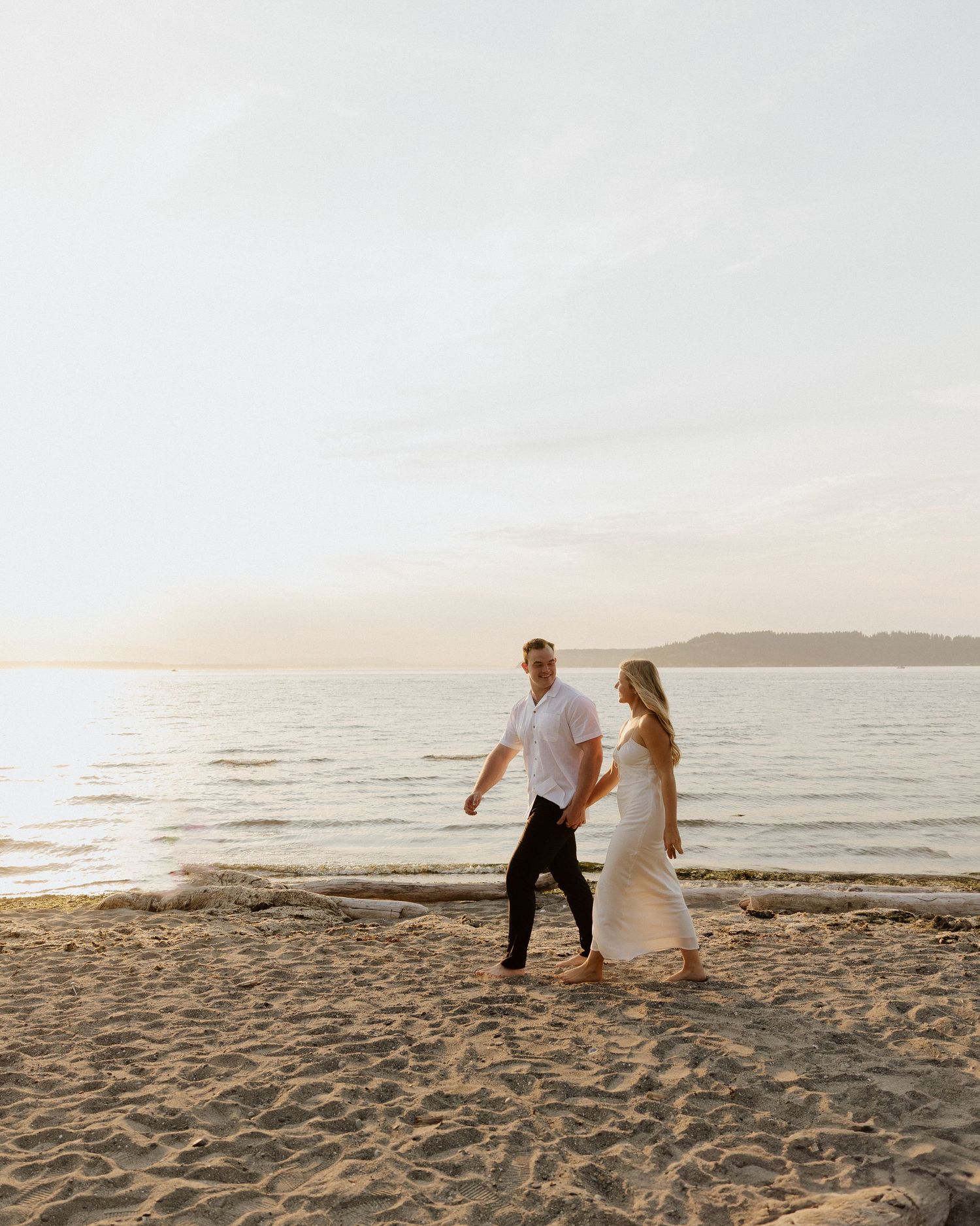 A couple strolls along the shoreline during golden hour with waves in the background.