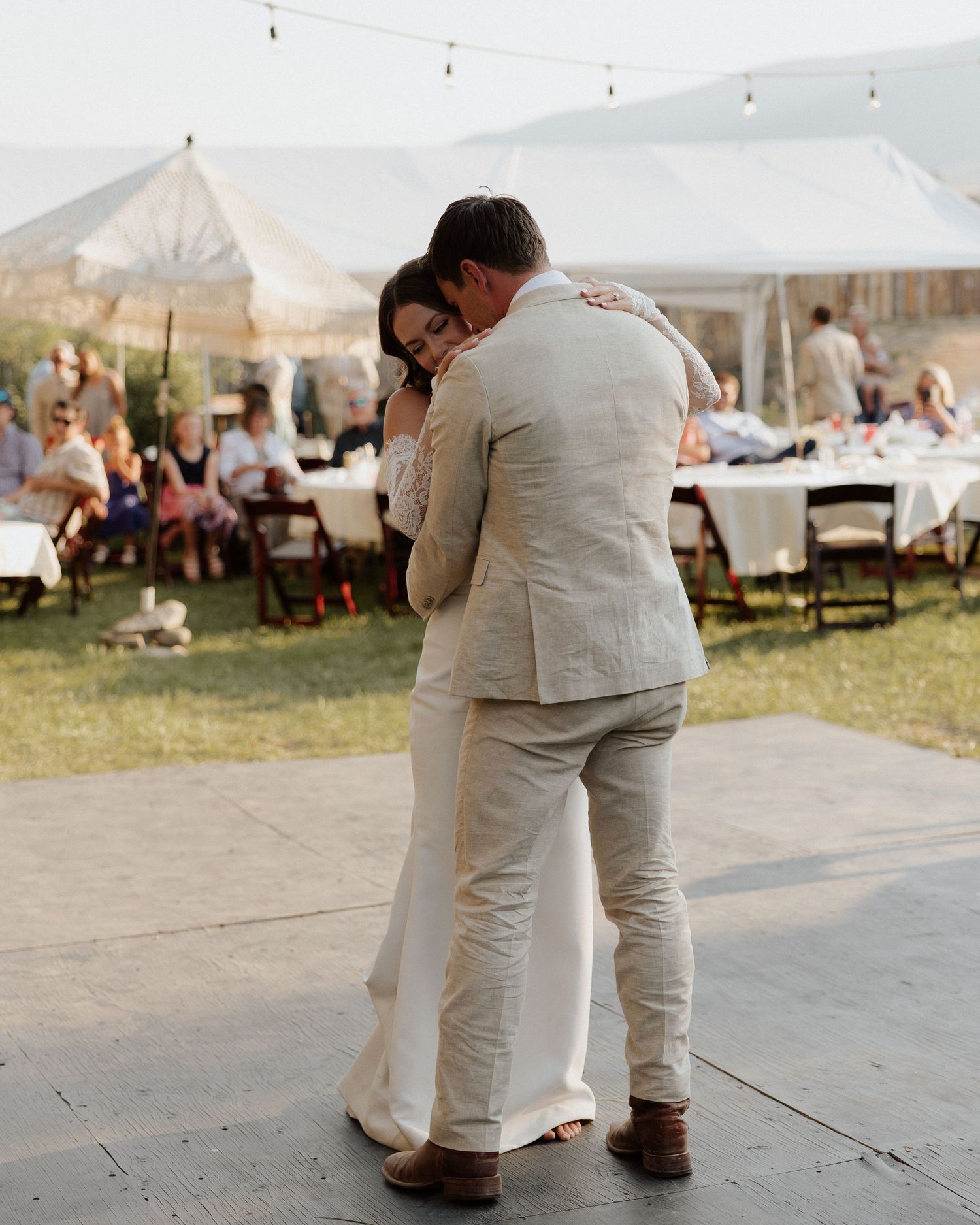 Couple embracing during their first dance at an outdoor wedding reception with a tent in the background.