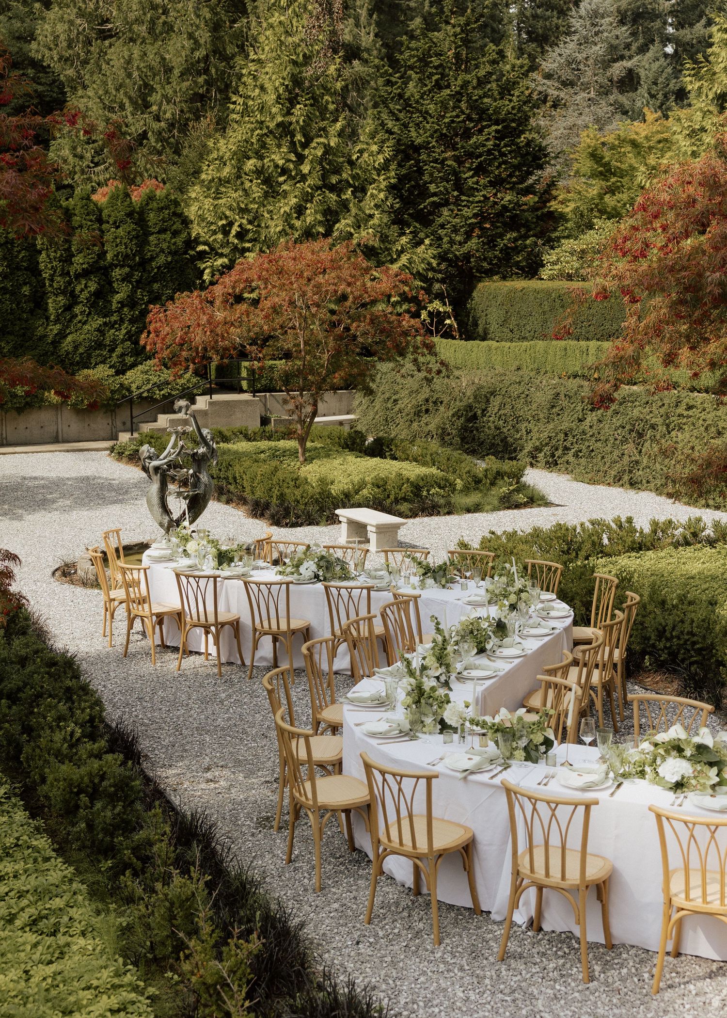 Elegant outdoor wedding reception tables with greenery garlands set in a formal garden with autumn foliage.