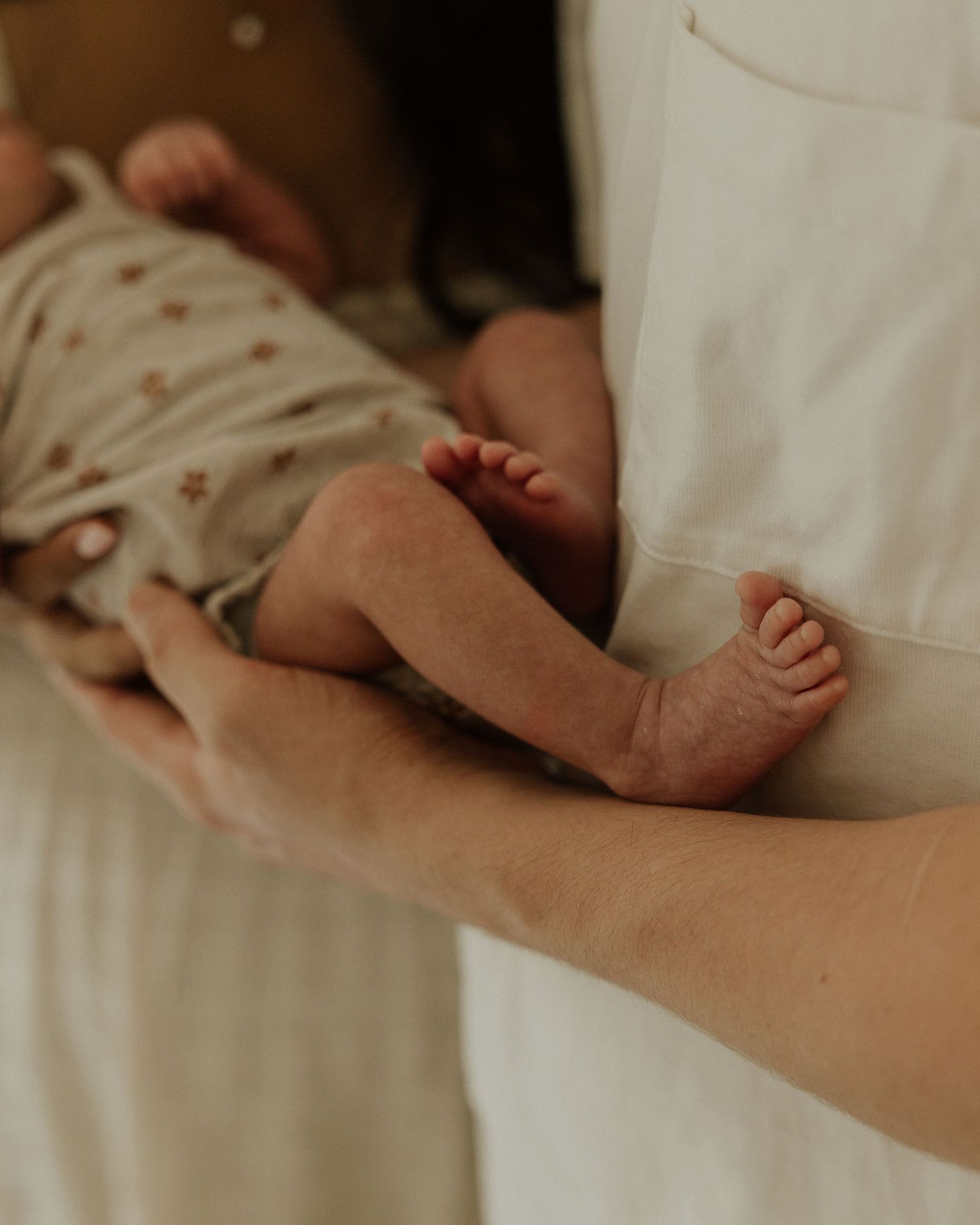 Close-up of tiny newborn baby feet and legs resting on parent's arm.