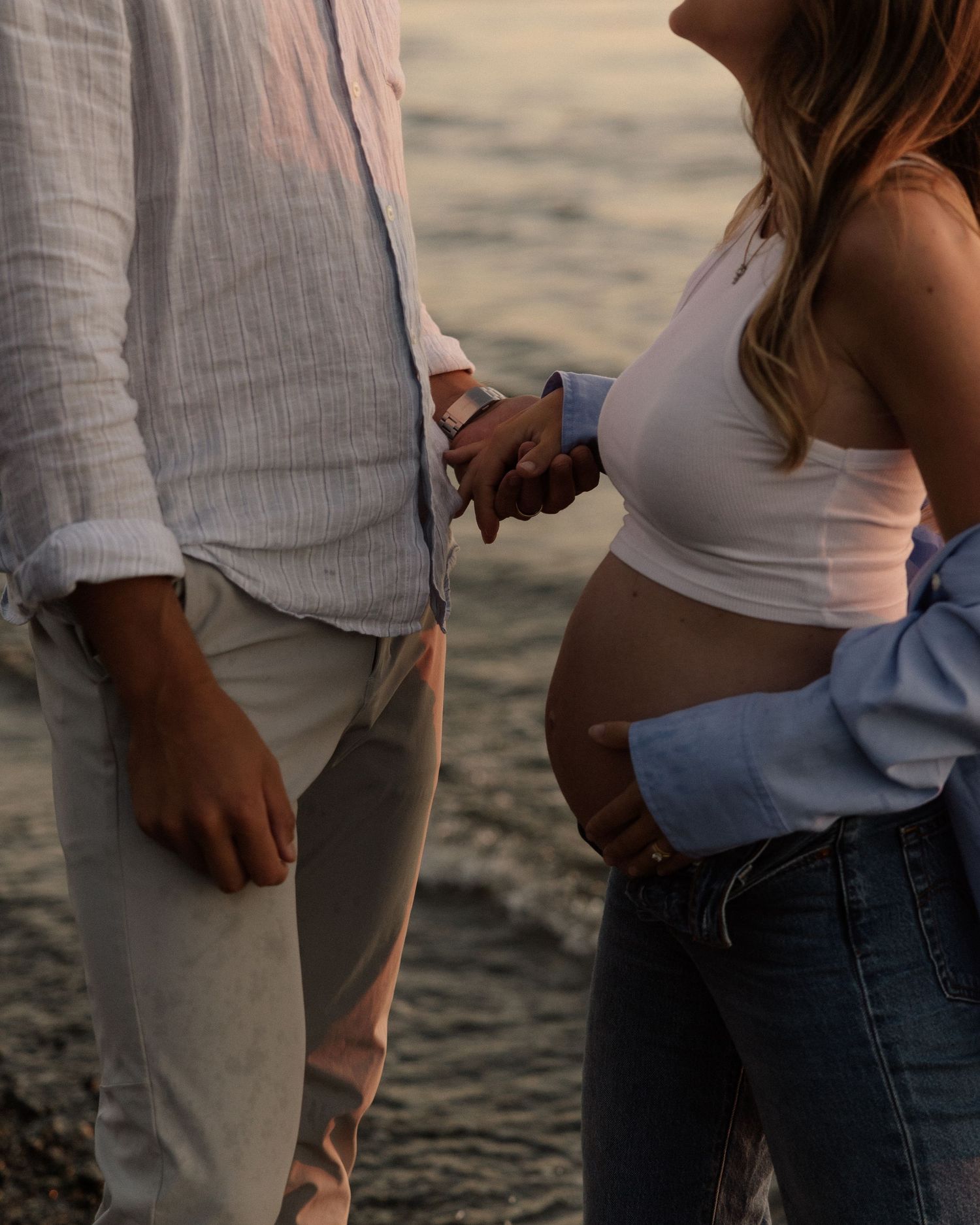 An expectant couple shares a tender moment on the beach at sunset.