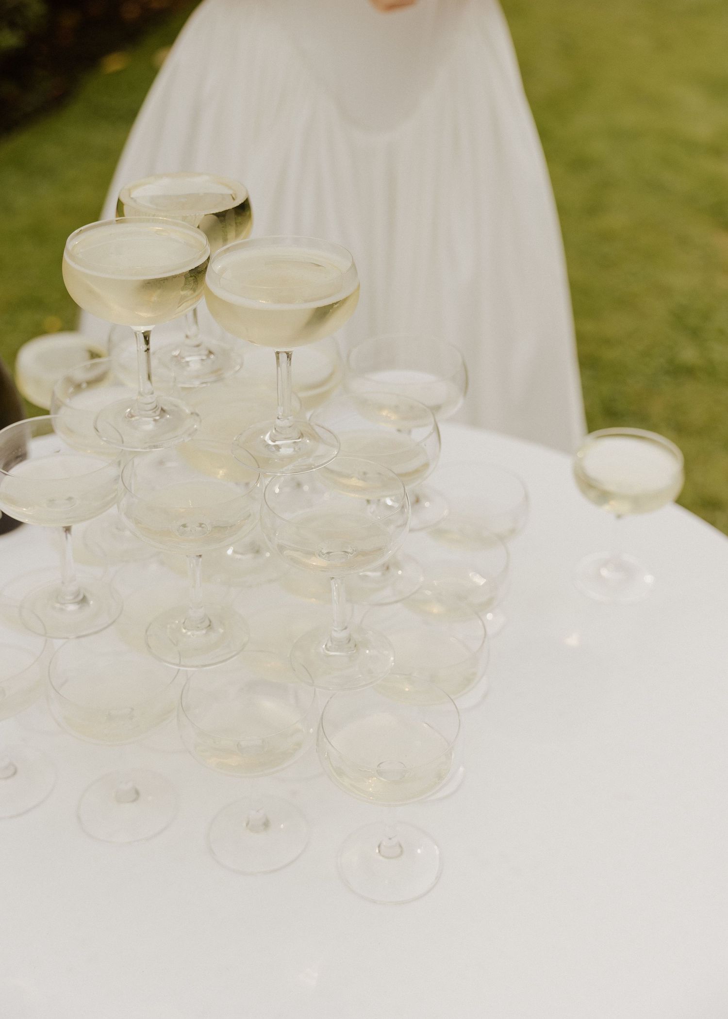 Elegant champagne tower with coupe glasses at a white-themed wedding reception.