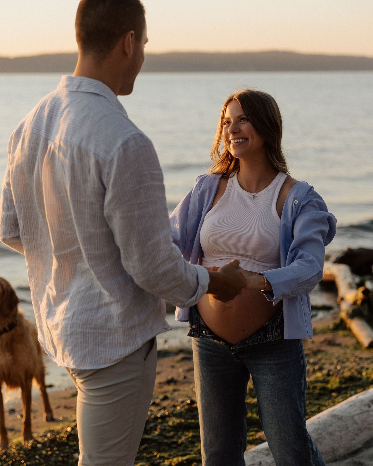 Maternity photoshoot on rocky beach at sunset with dog in background.