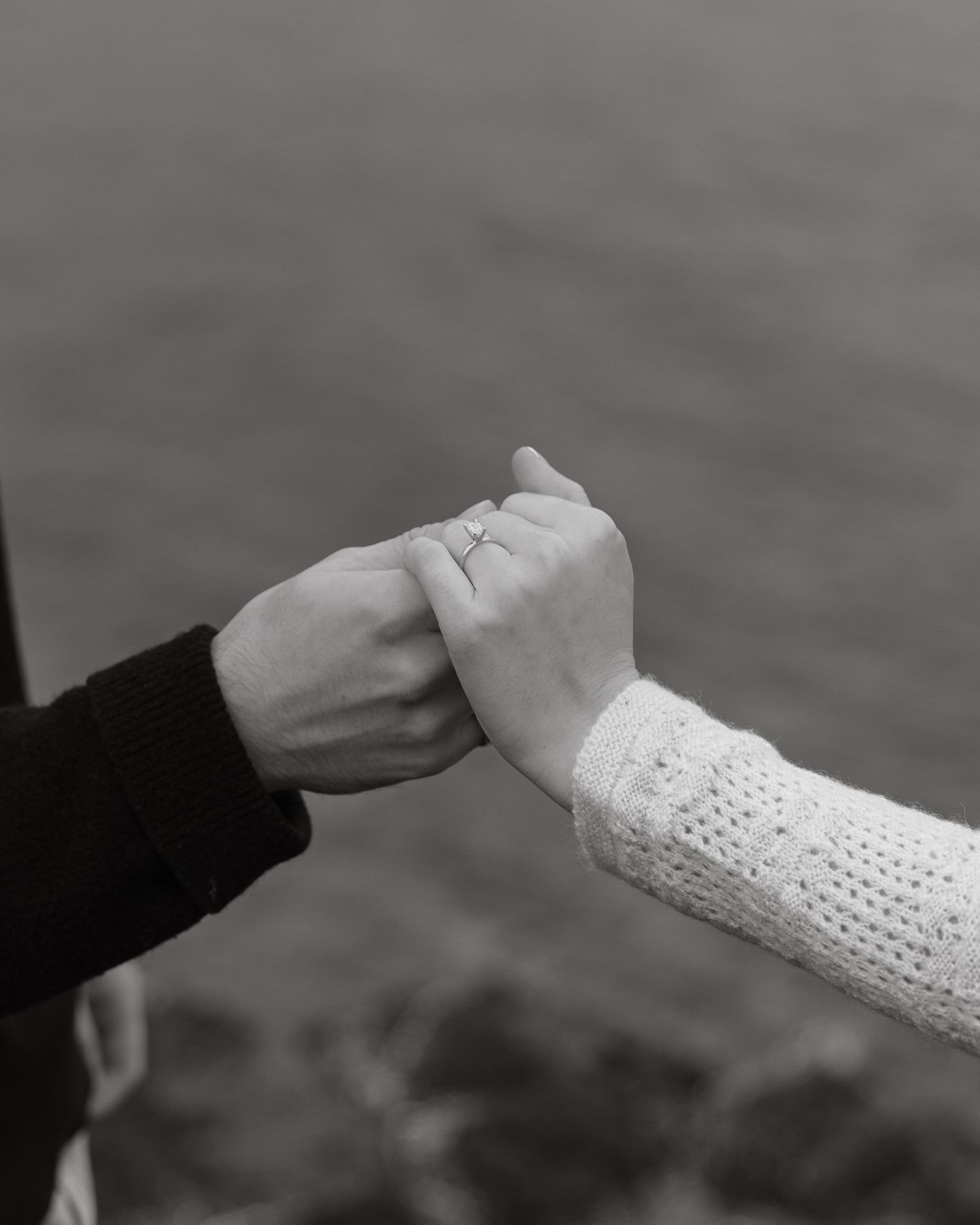 Close-up black and white photograph of two hands clasped together against water backdrop.