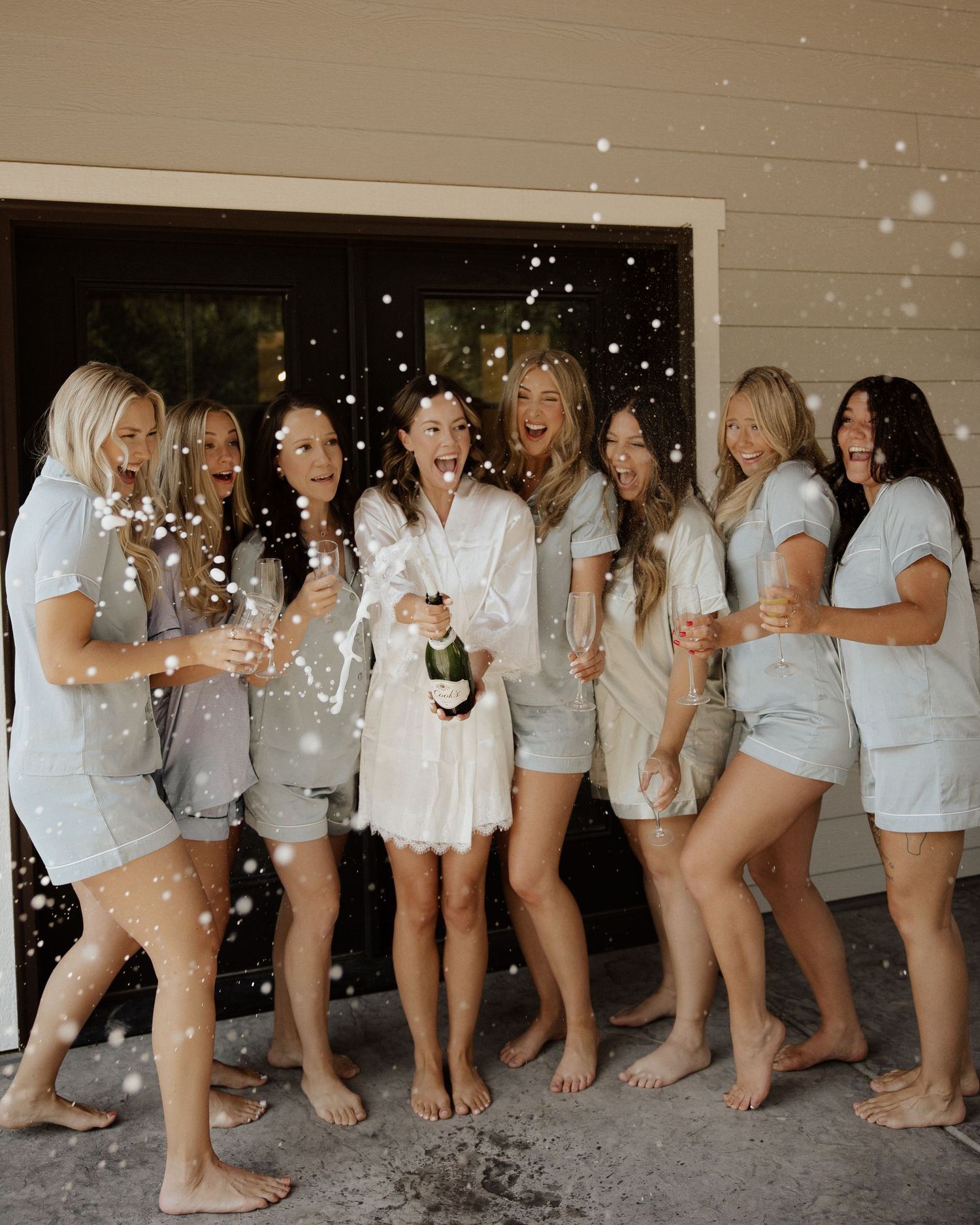 Bridesmaids in matching white outfits celebrate with champagne and confetti.