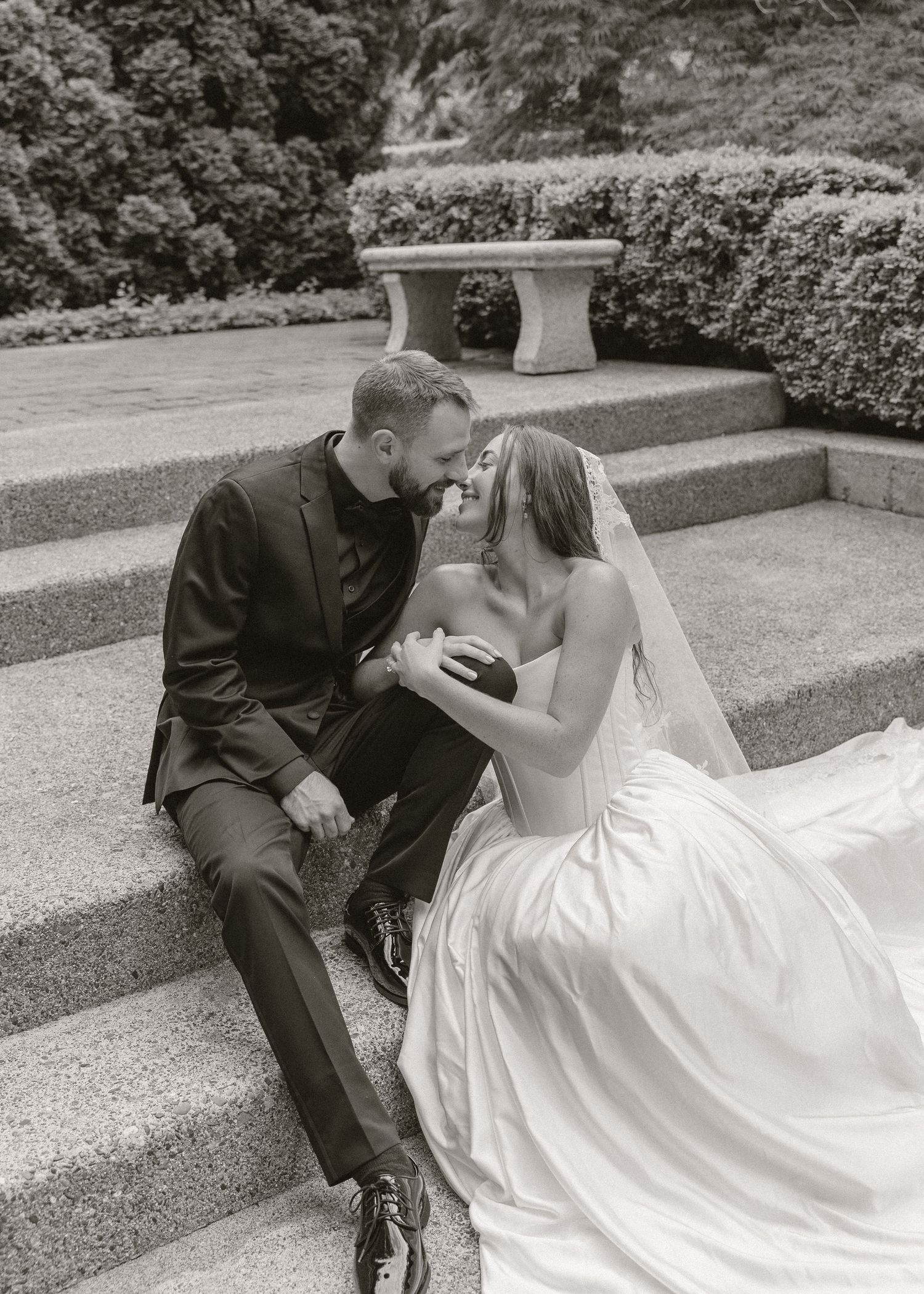 Black and white photo of bride and groom sitting on stone steps sharing a romantic moment.